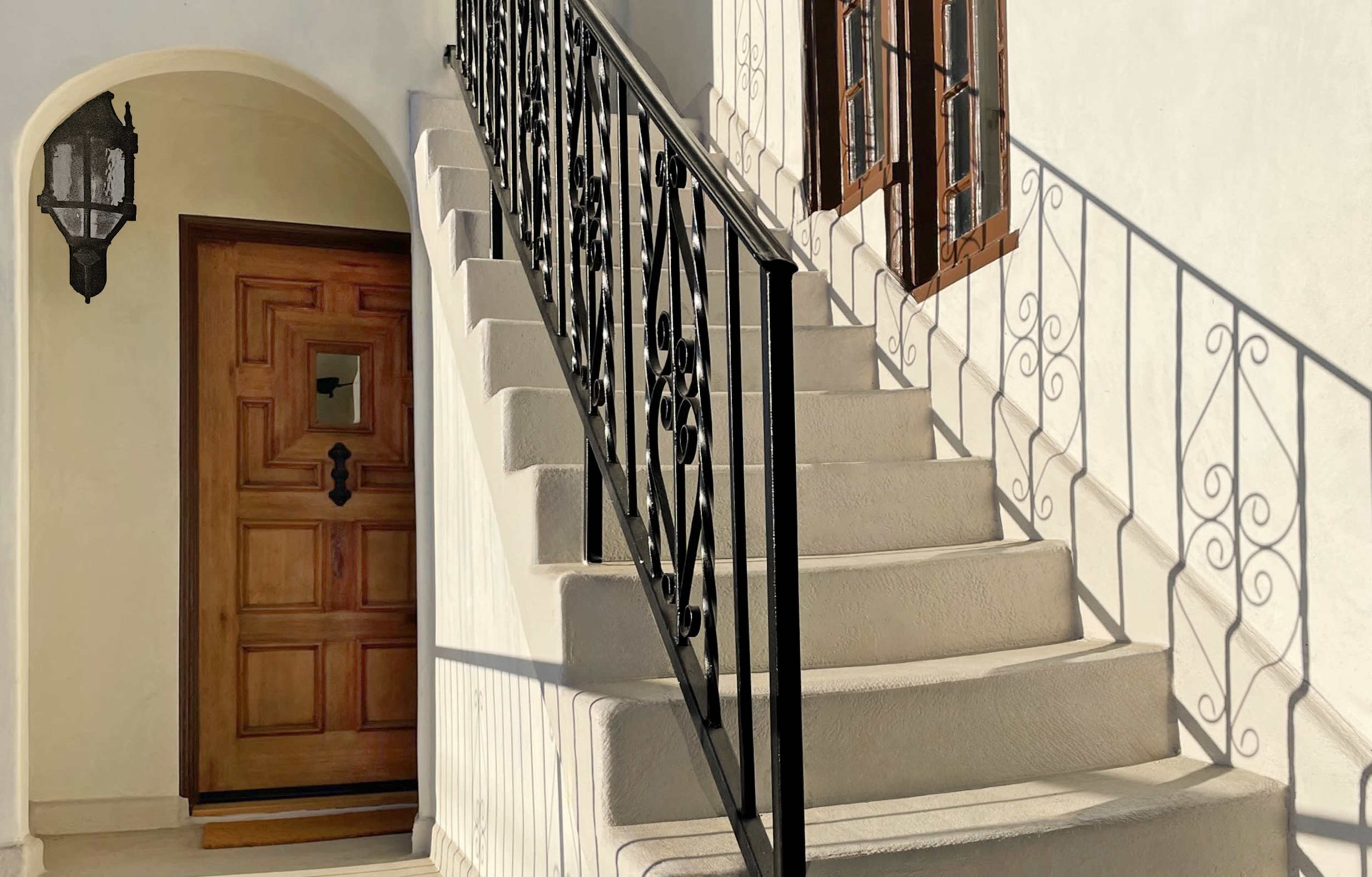 The image shows a set of stone steps leading up to an arched doorway with a wooden door and ornate black railing.