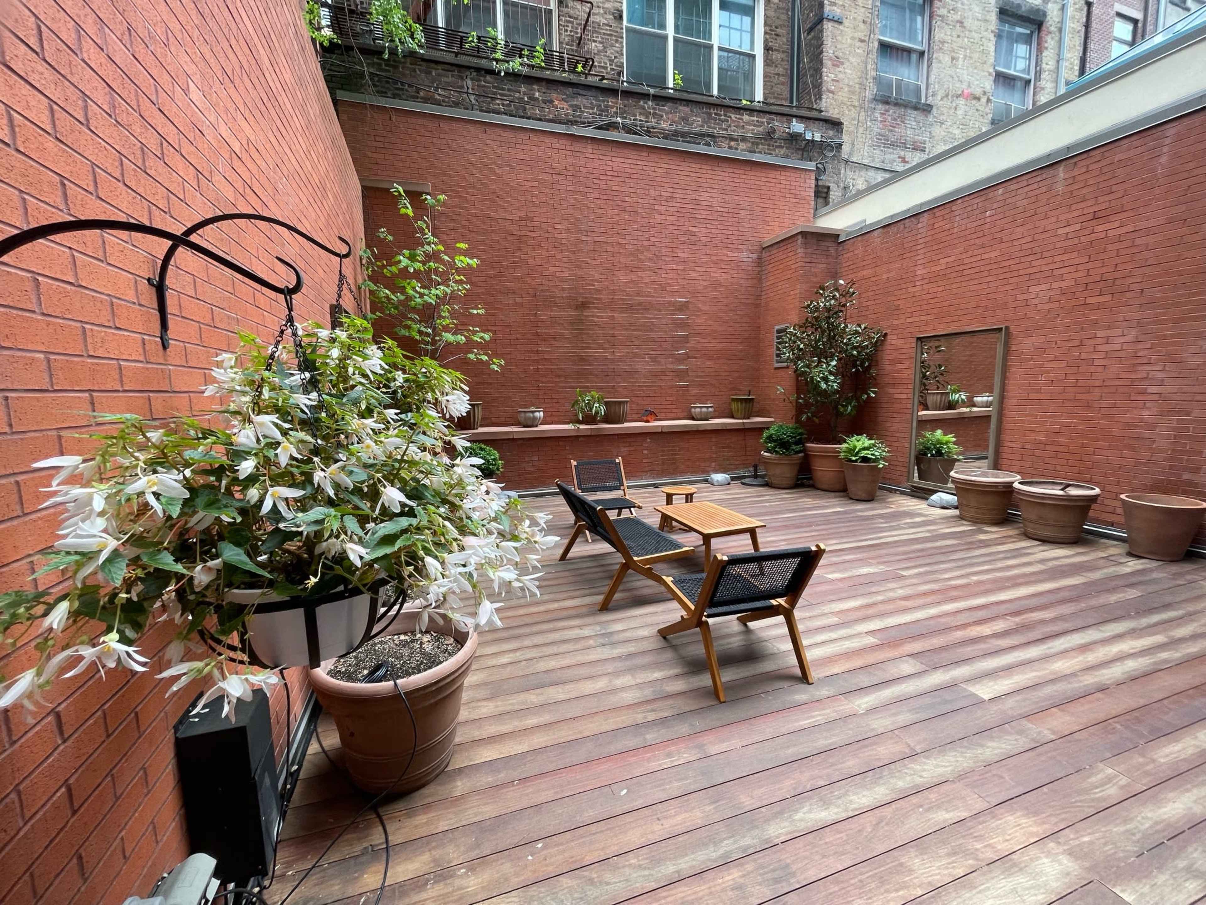 A wooden deck area with potted plants and seating arrangements in a brick-walled courtyard.