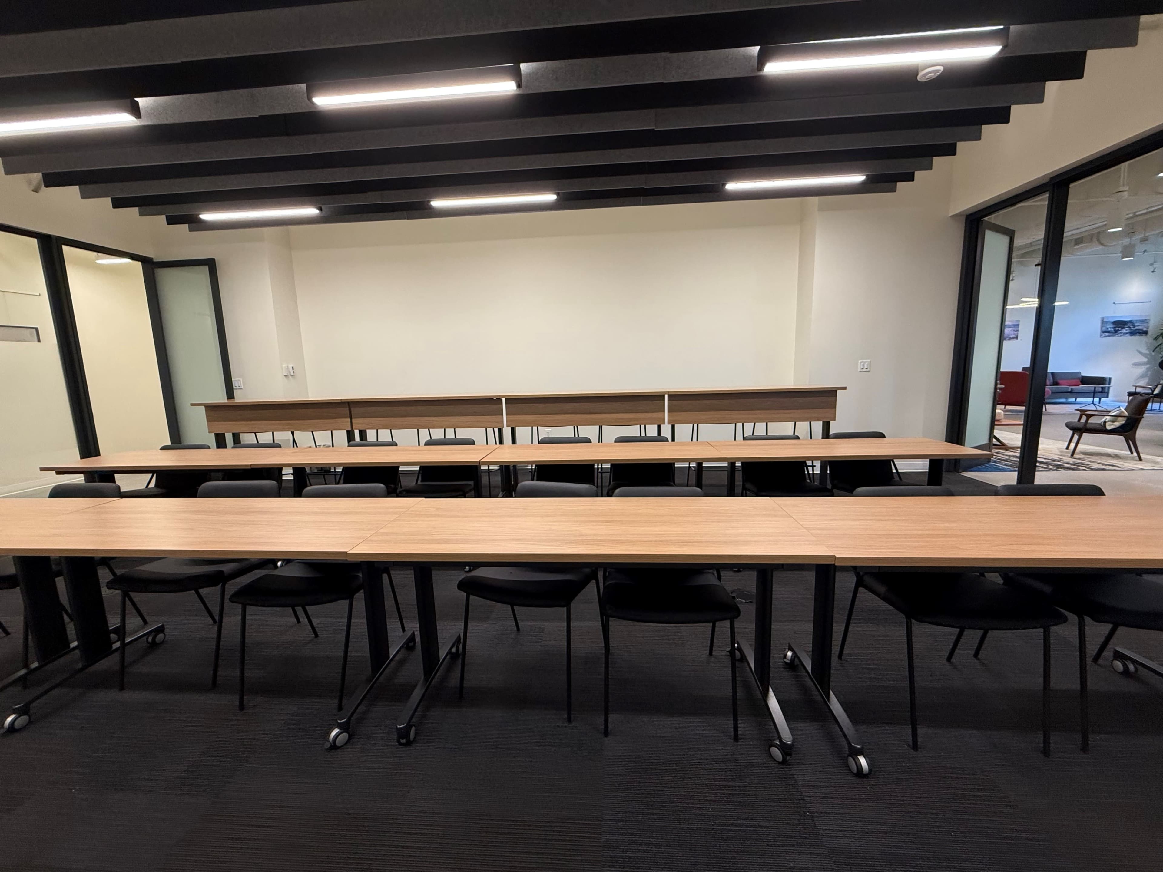 The image shows a modern conference room with long, rectangular tables arranged in rows and black chairs positioned around them.