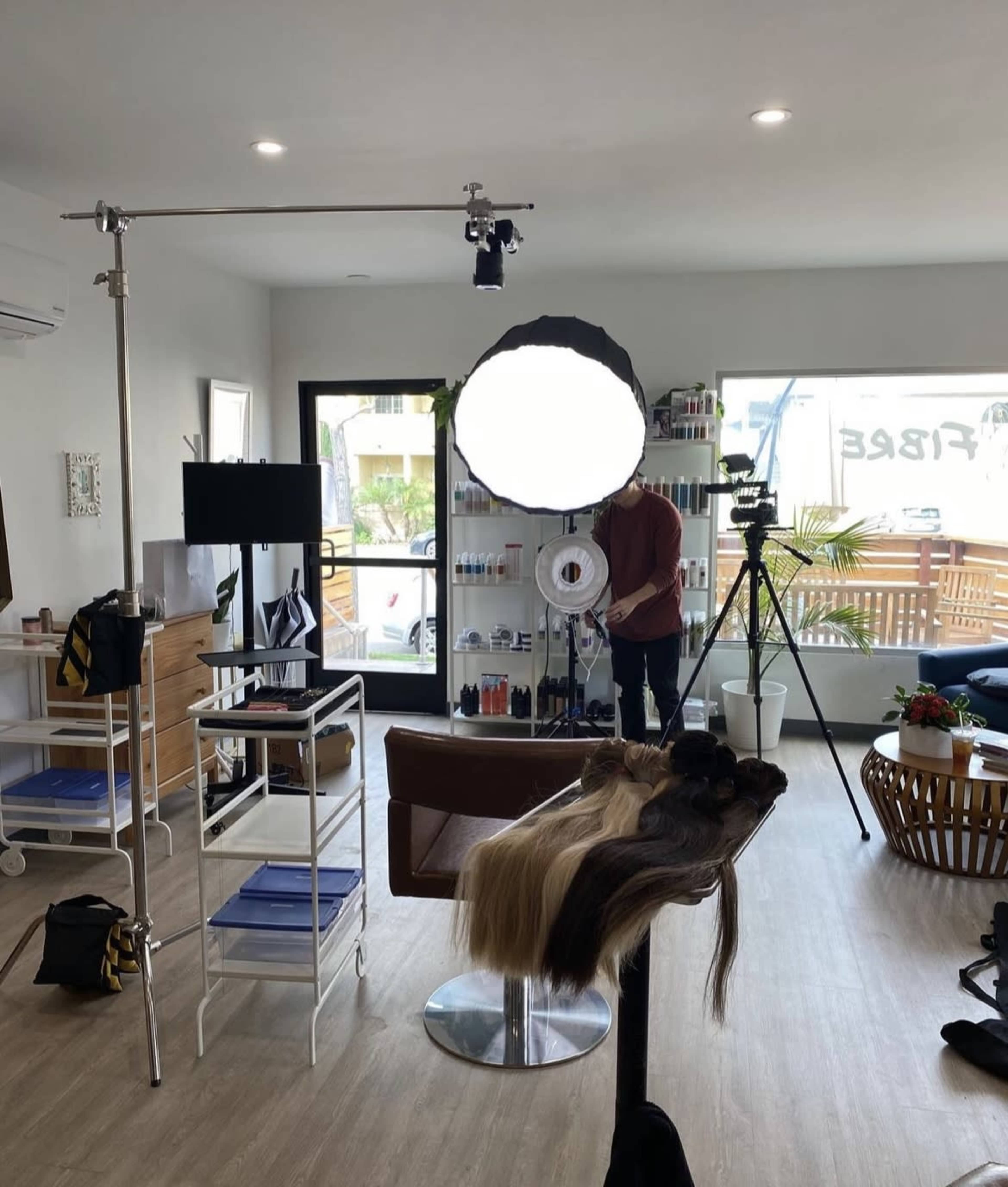 A modern hair salon interior with a styling station, a large ring light setup, and hair extensions placed on a work surface.