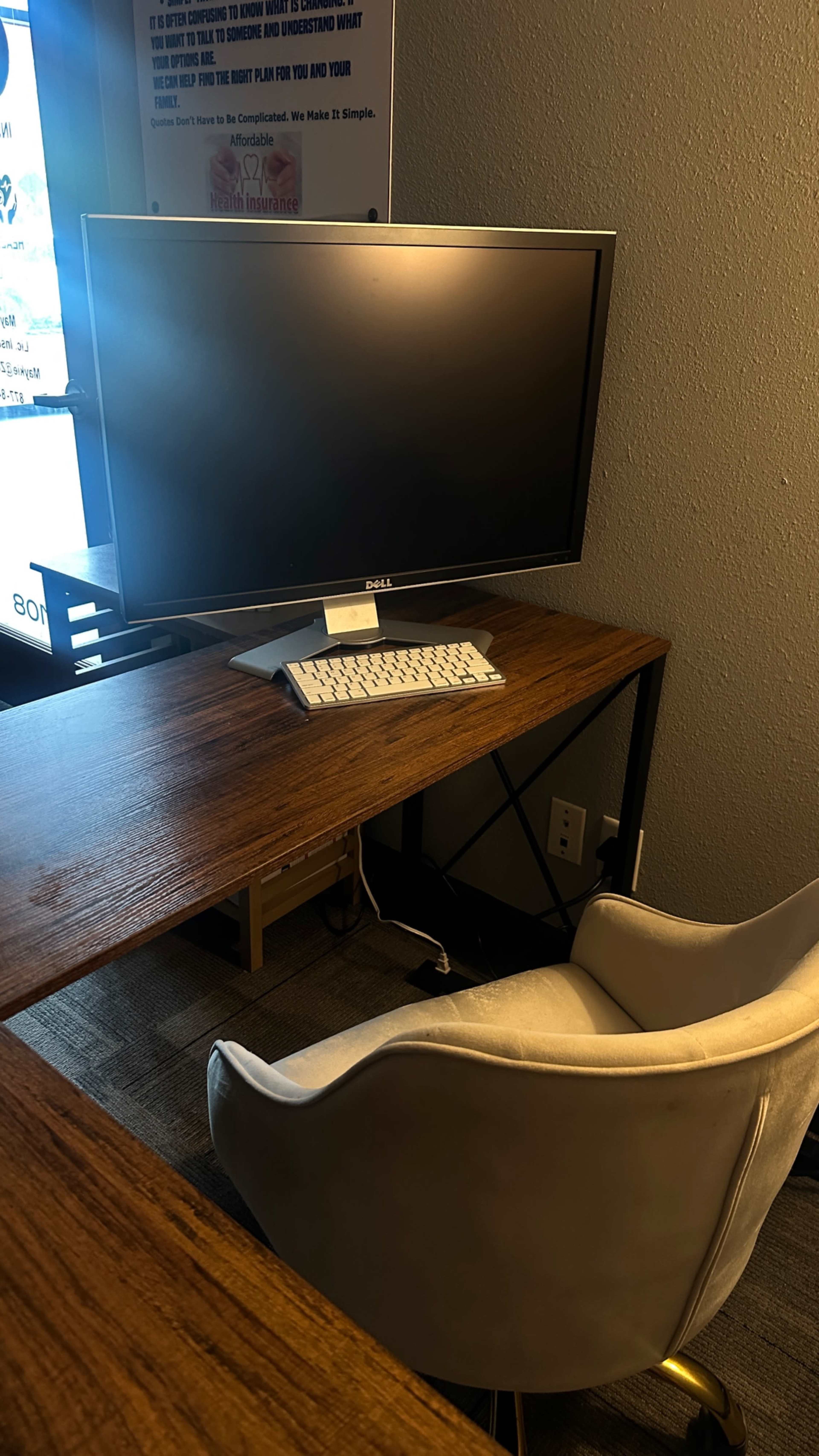 A desk with a monitor and keyboard is positioned next to a white chair in a workspace setting.