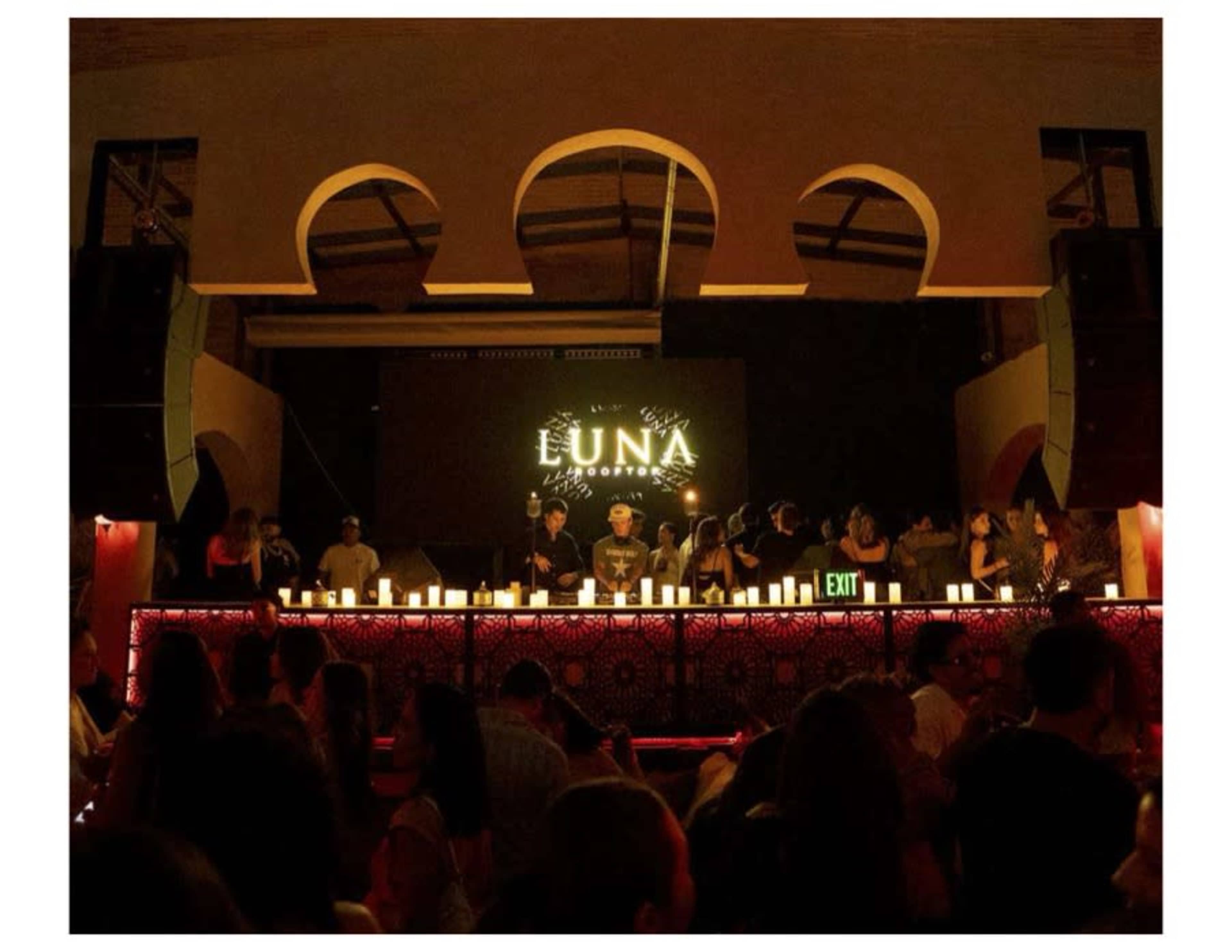 A busy nightclub scene features a DJ performing on stage with a lit sign reading "LUNA," while people dance and socialize in the foreground.