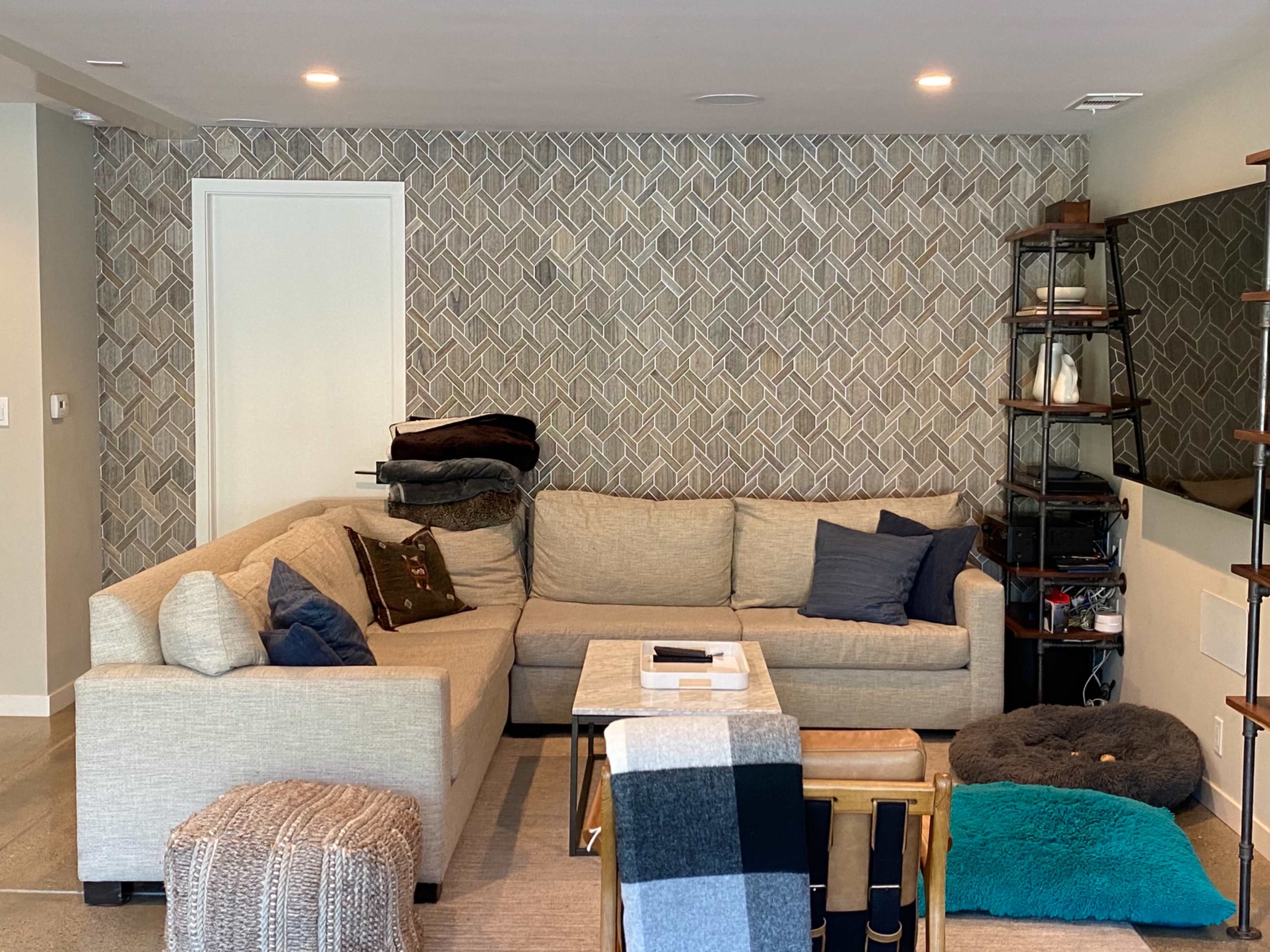 A cozy living room featuring a sectional sofa with various cushions, a coffee table, and a shelf against a patterned wall.