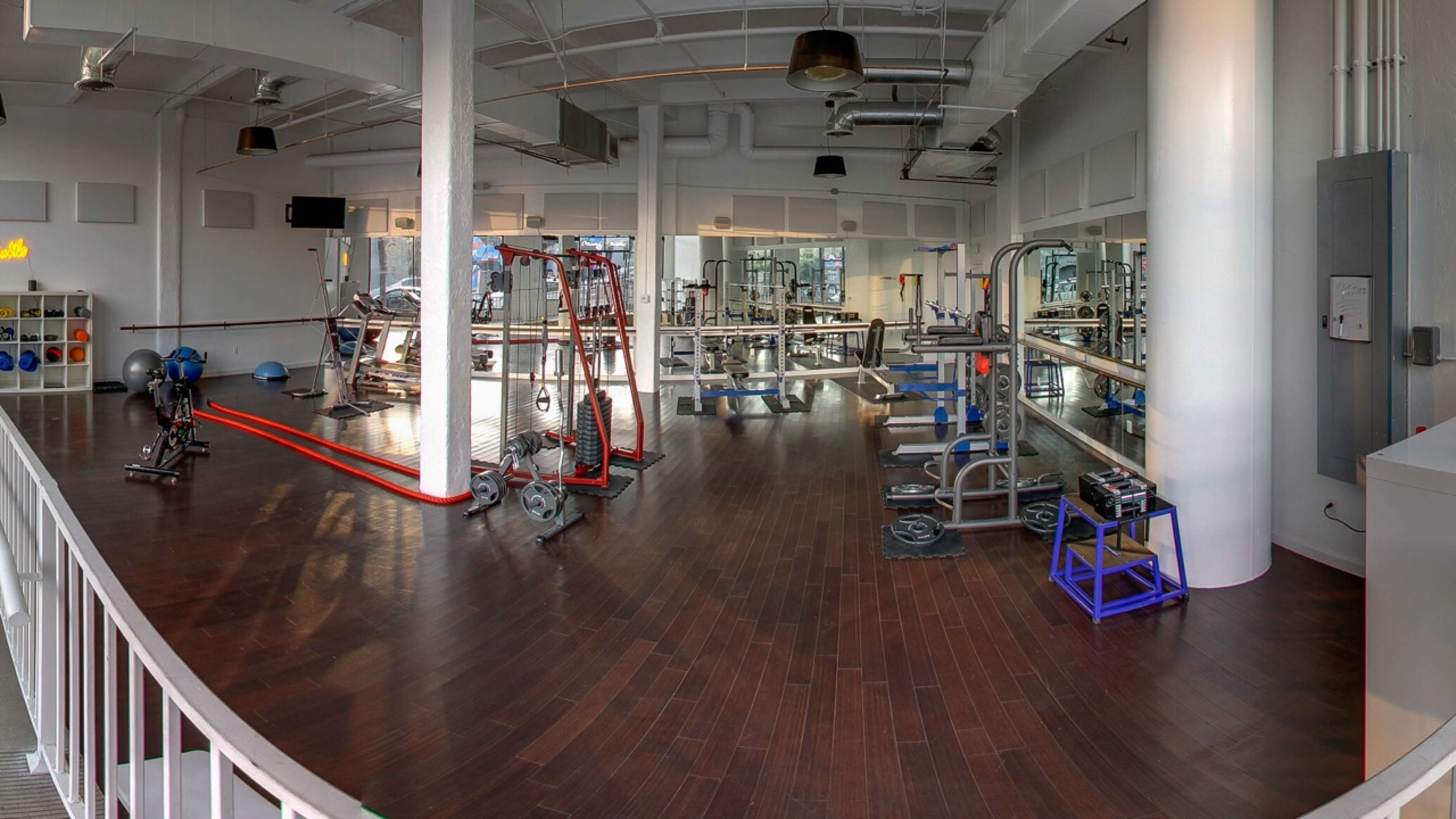 A spacious gym interior with various exercise equipment arranged on polished wooden floors.
