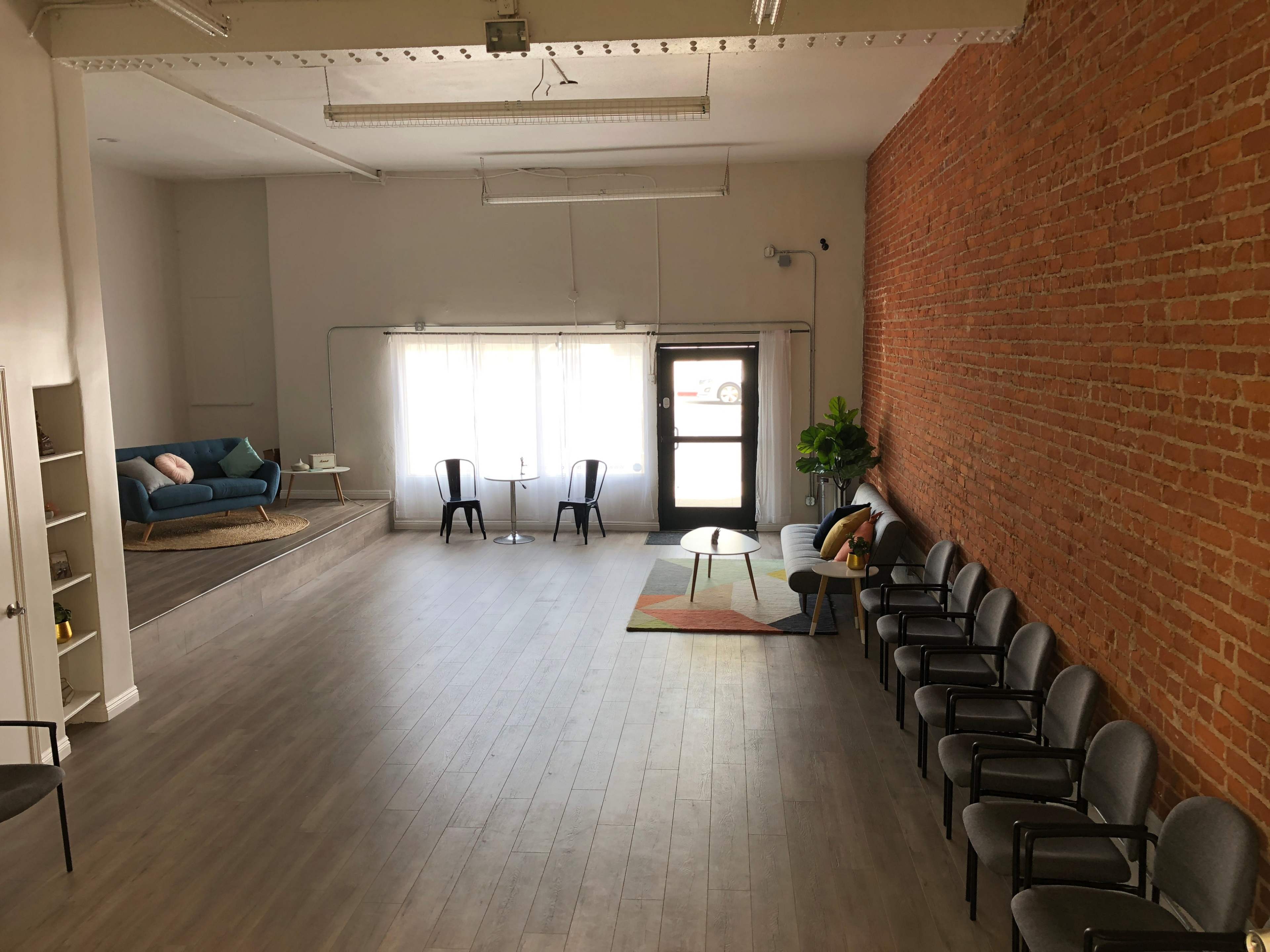 A spacious room with a brick wall, a seating area with chairs along one side, a coffee table and couch, and large windows allowing natural light.
