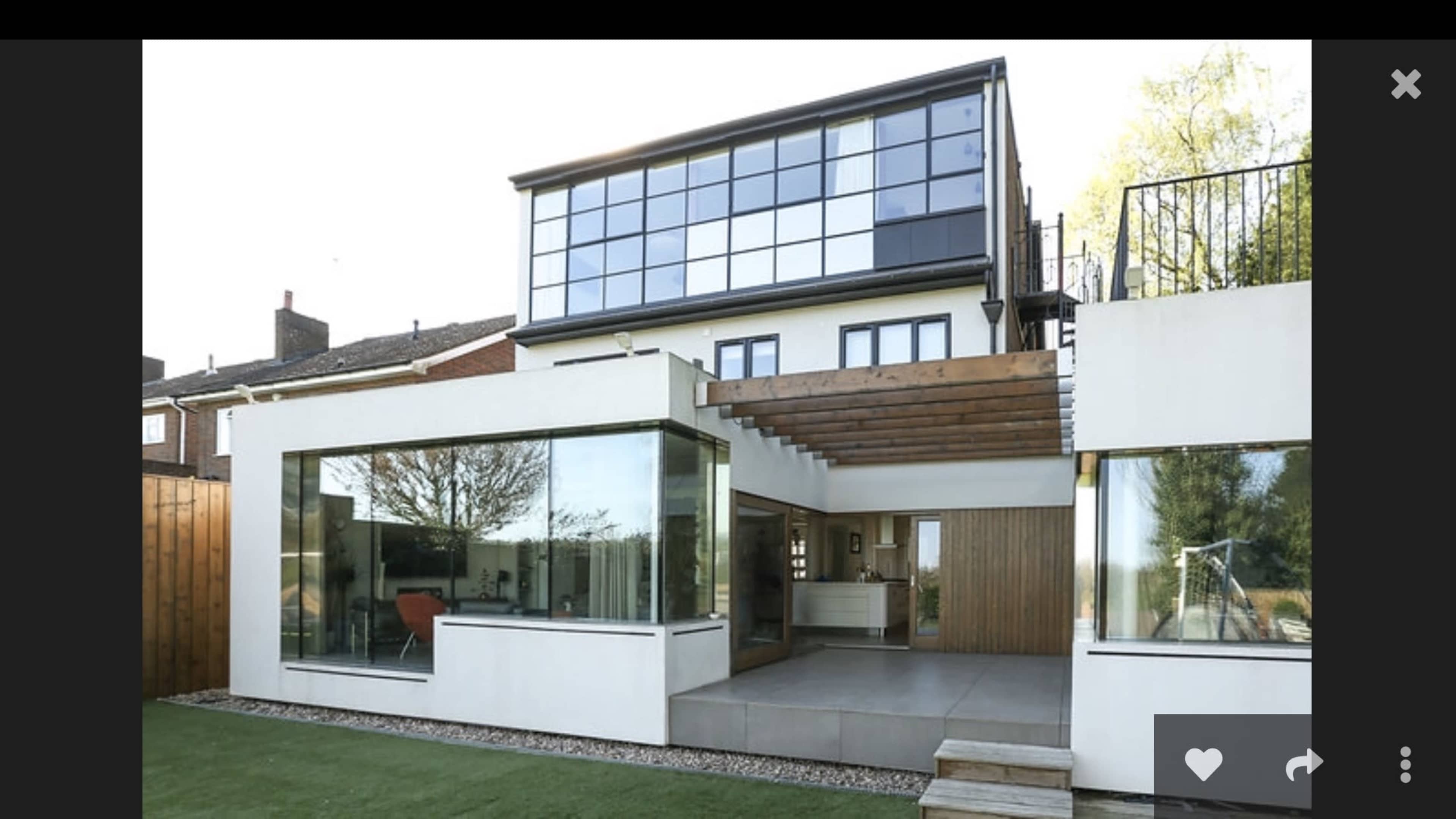 A modern two-story house with large glass windows and a spacious patio area surrounded by a well-maintained lawn.