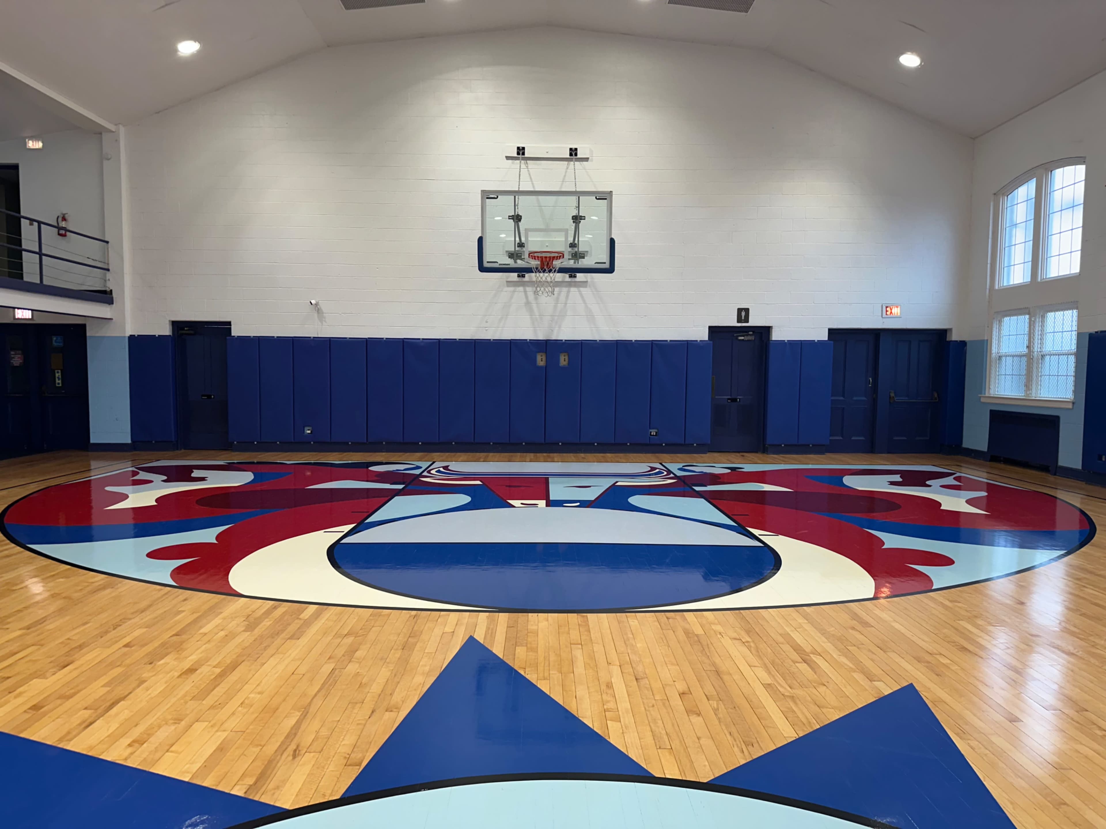 The image shows a basketball court with a colorful logo at center court and a hoop at one end, surrounded by blue walls.