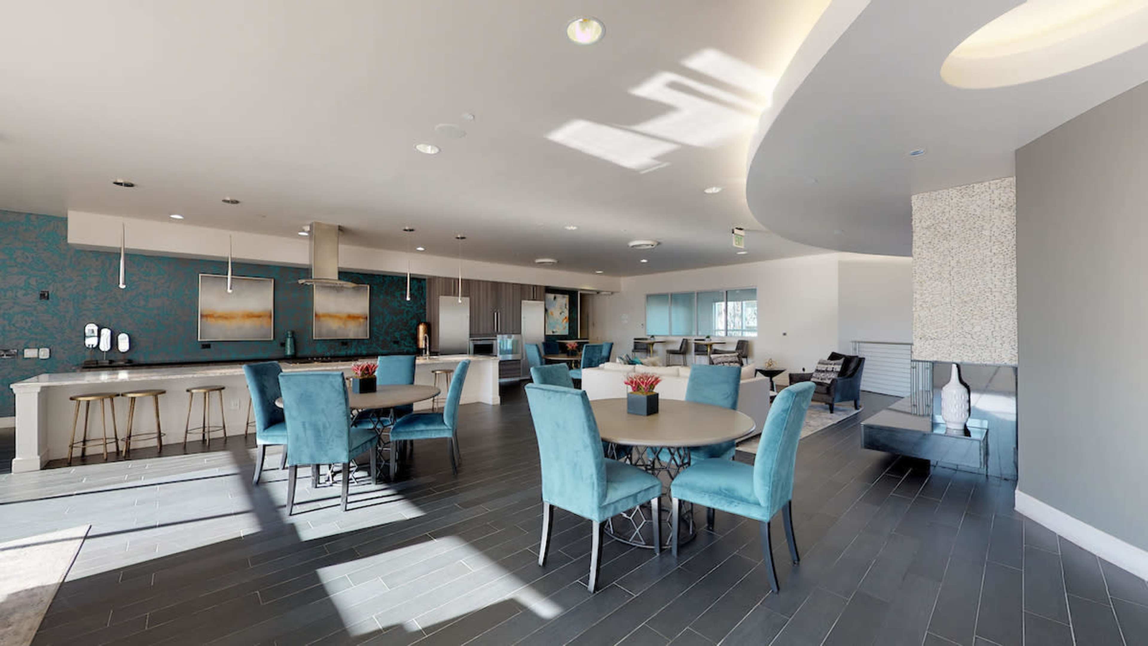 A modern lounge area with blue seating, circular tables, and a kitchen space in a well-lit open layout.