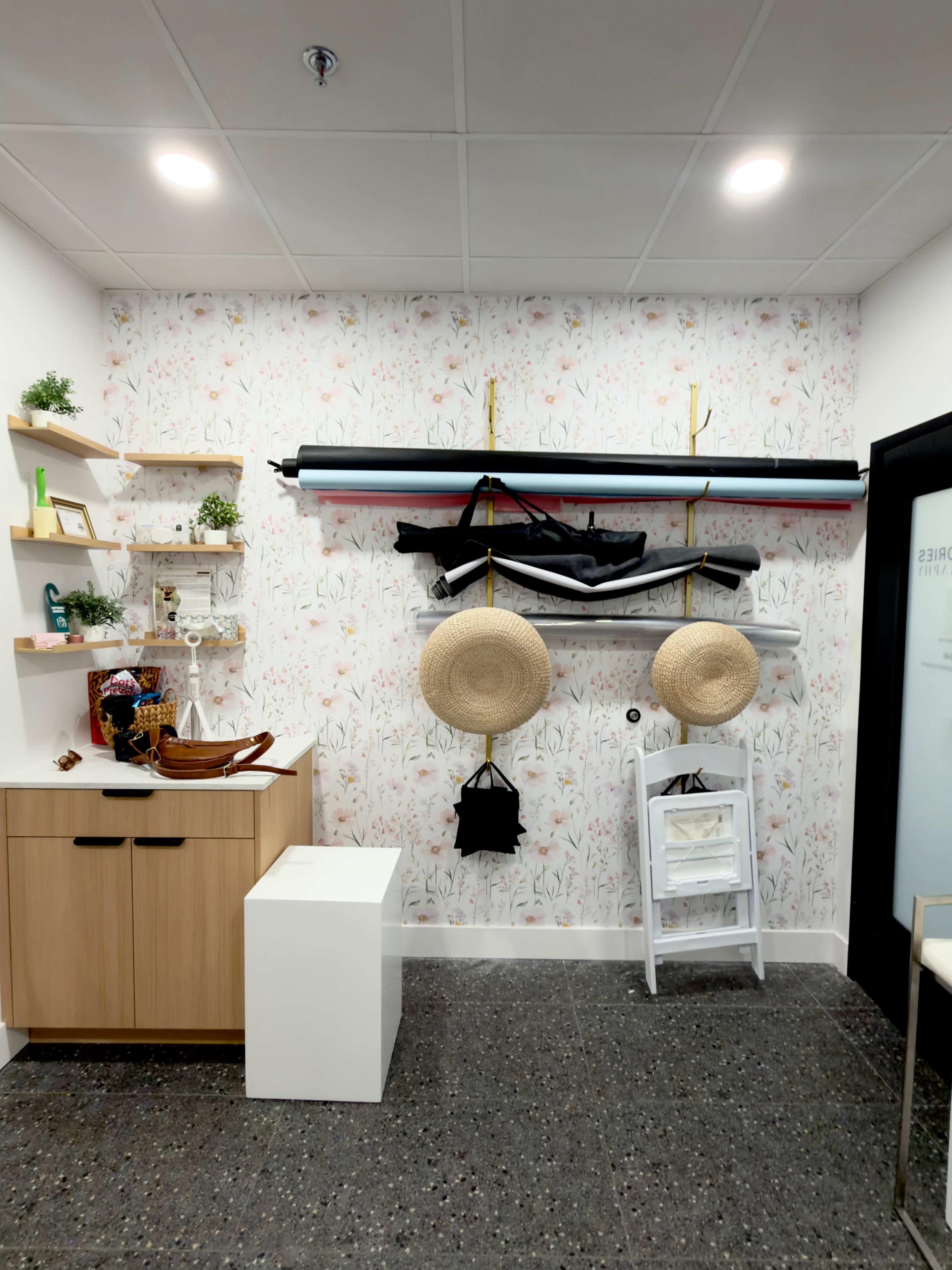 The image shows a small room with floral-patterned wallpaper featuring storage solutions, including shelves, hanging hats, and mounted items such as what appears to be a kayak.