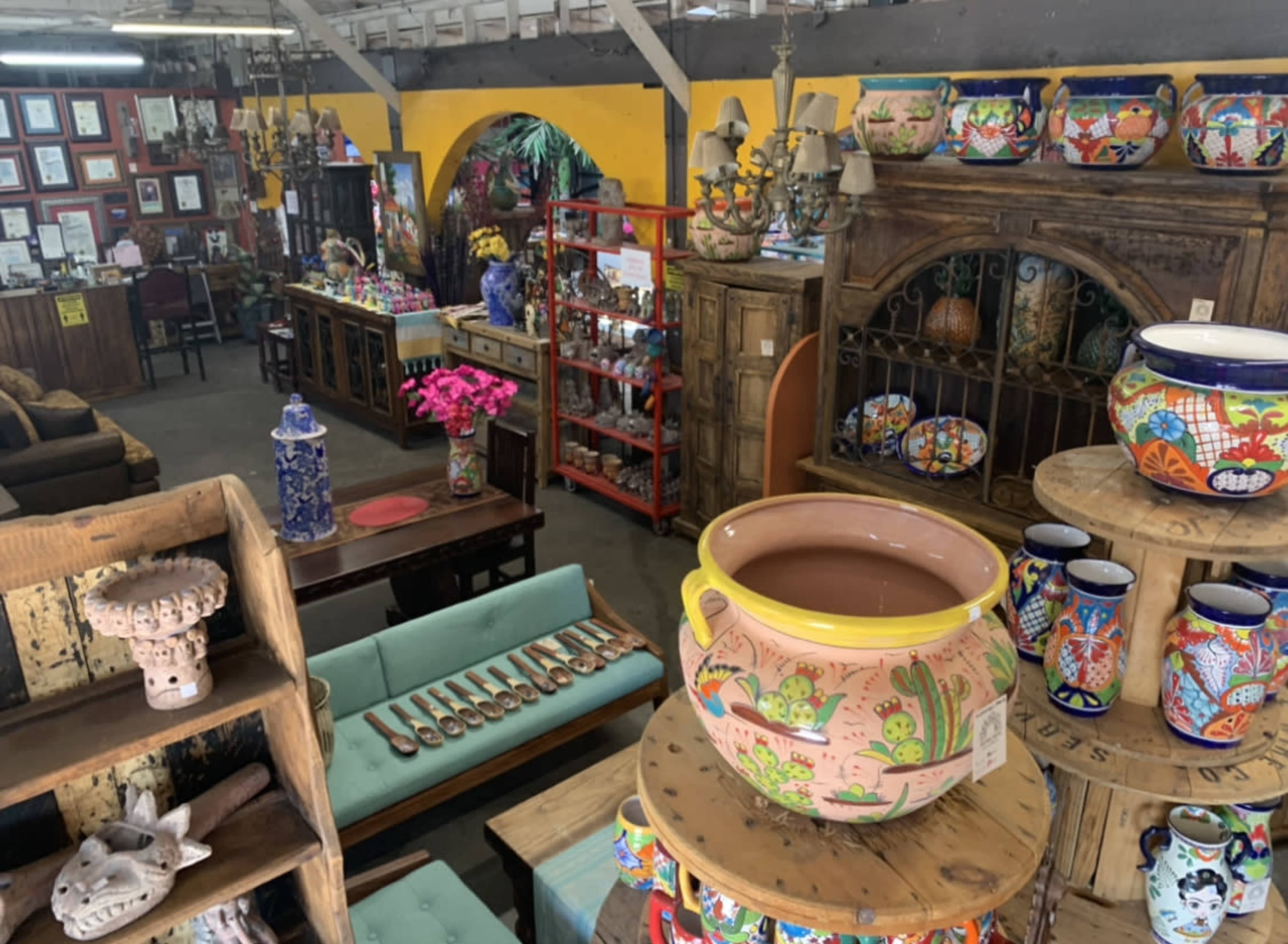 The image shows an interior of a store filled with various colorful pottery, wooden furniture, and decorative items set against a vibrant backdrop.