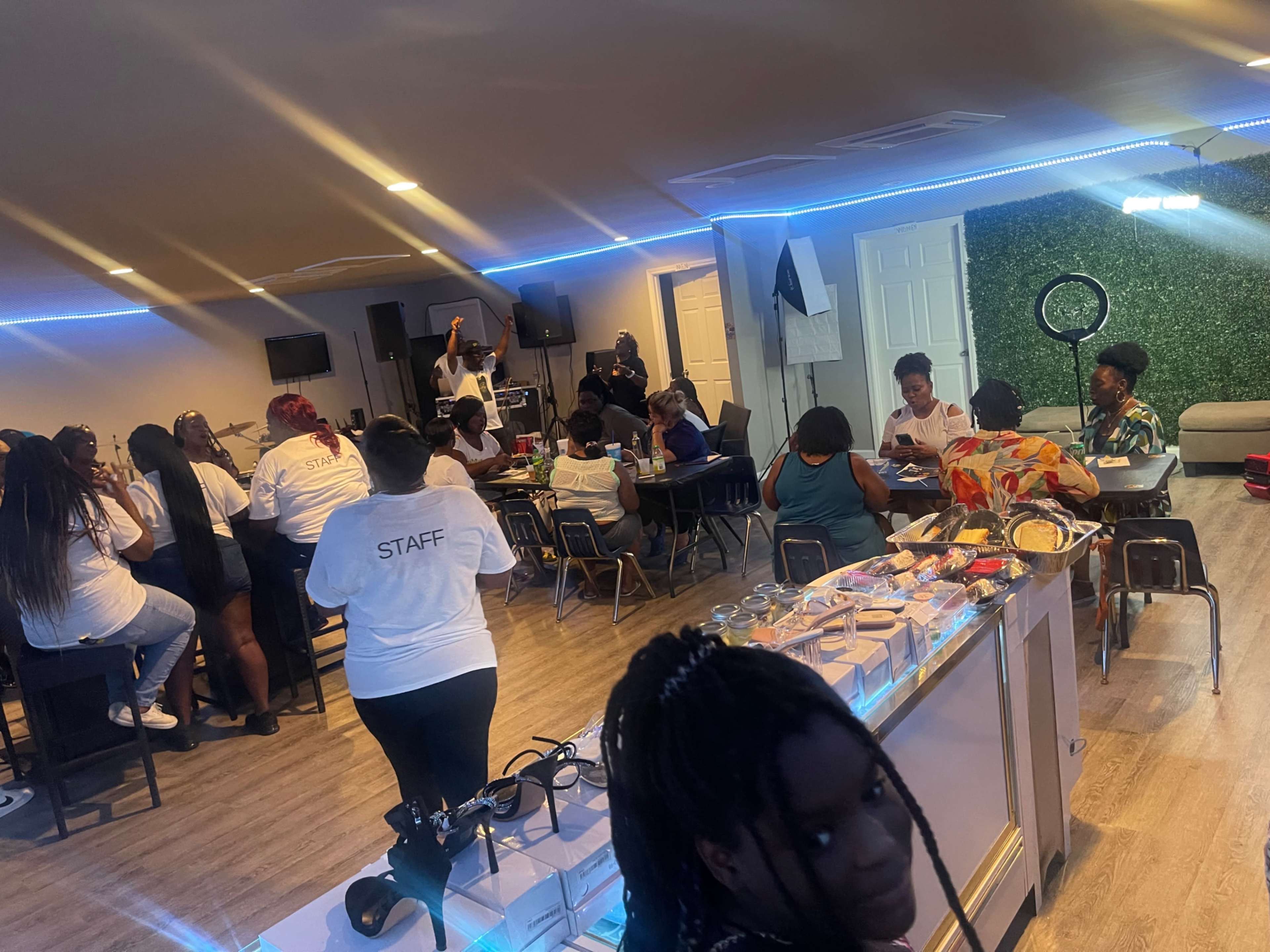 A group of people gathers in a spacious indoor venue, seated at tables and interacting, while some staff members are visible in white shirts.