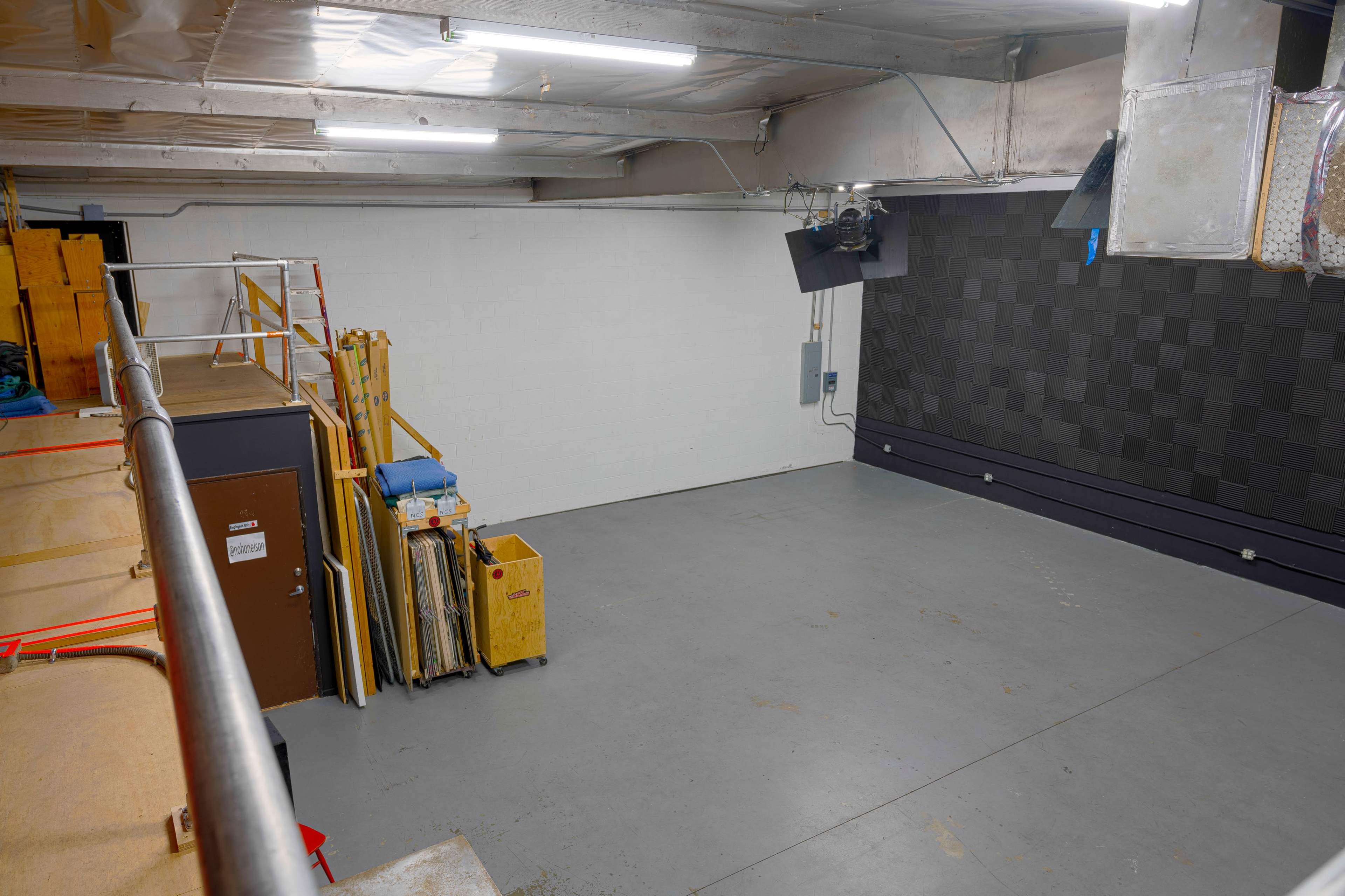 An empty industrial space with a gray floor, a bare white wall, and various equipment stored in the corner.