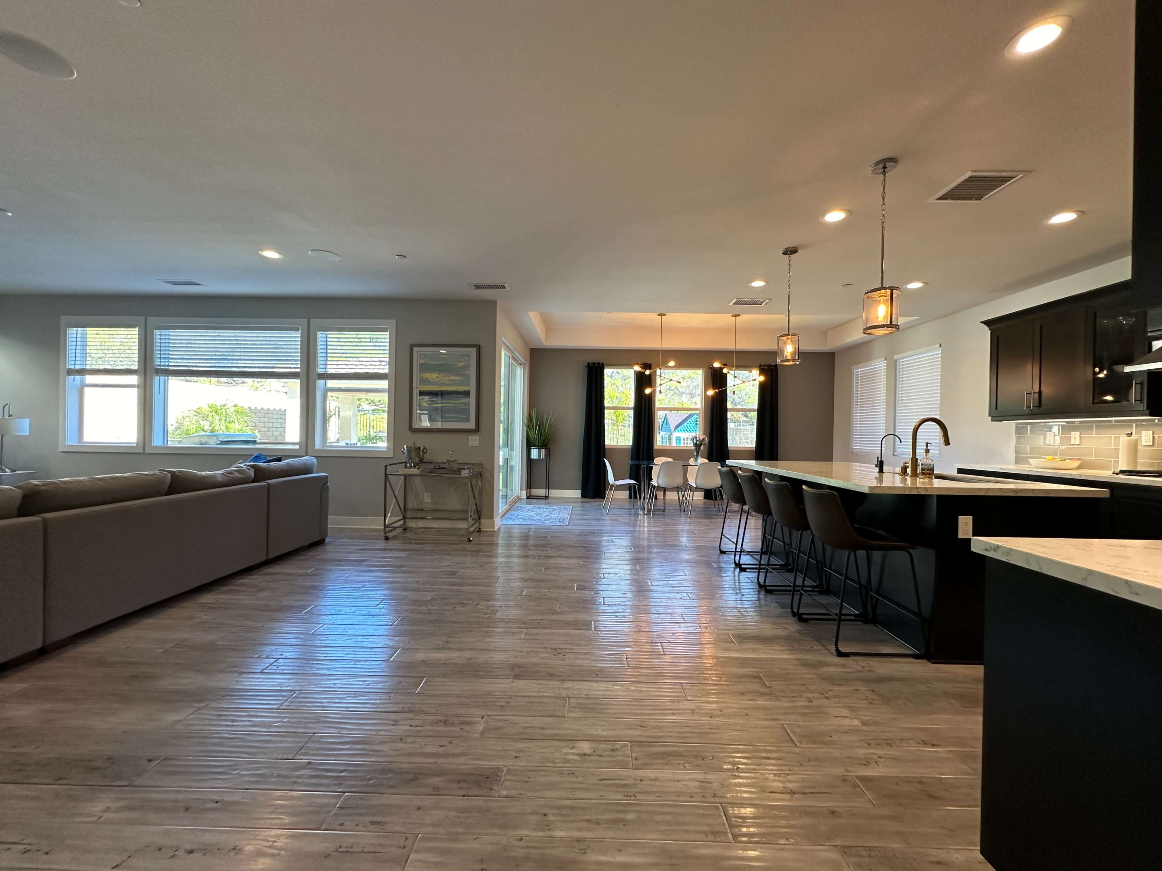 A spacious, modern living area with a kitchen island, bar stools, and large windows allowing natural light.