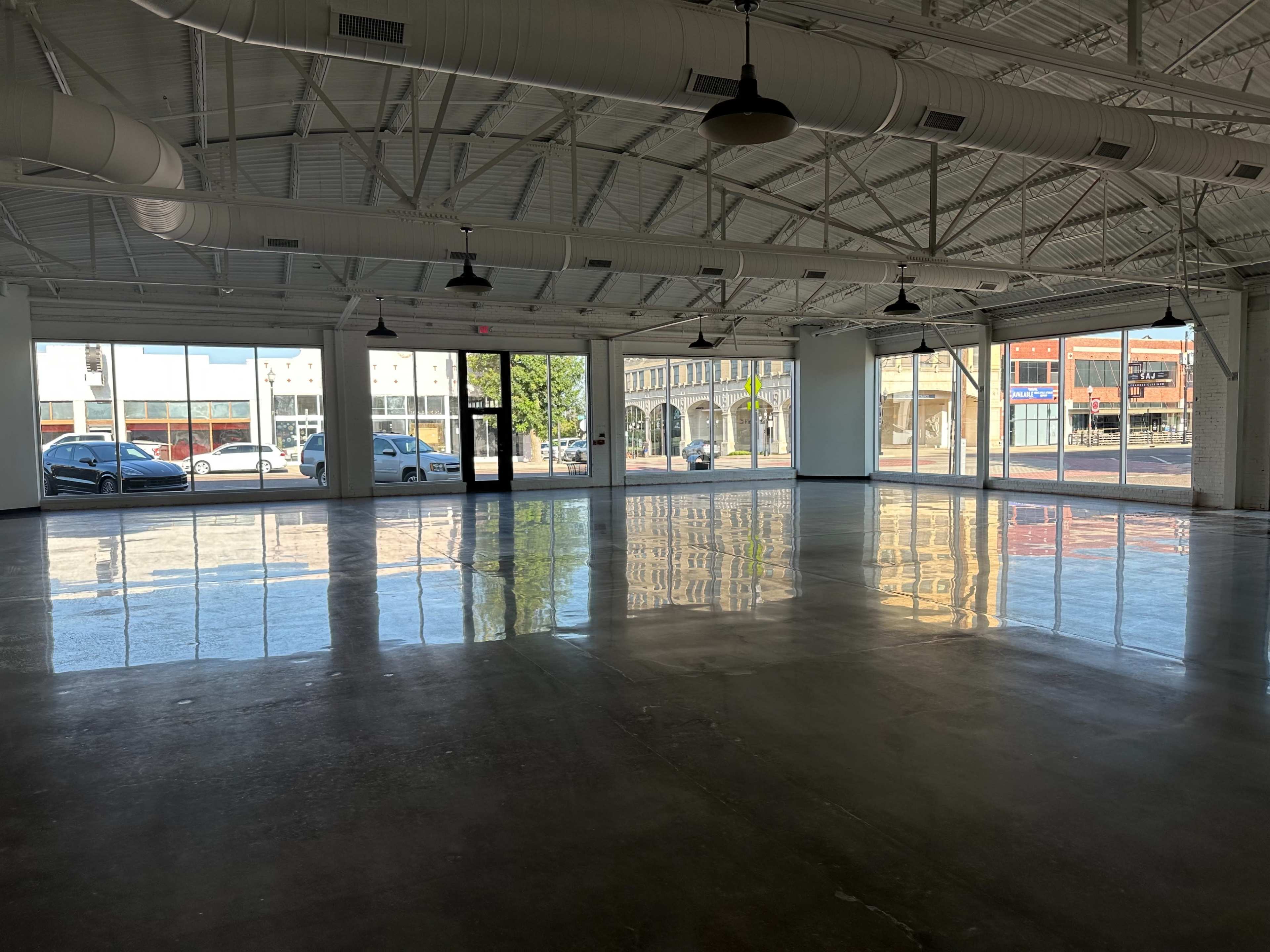An empty commercial space with polished concrete floors, large windows, and exposed ceiling beams.