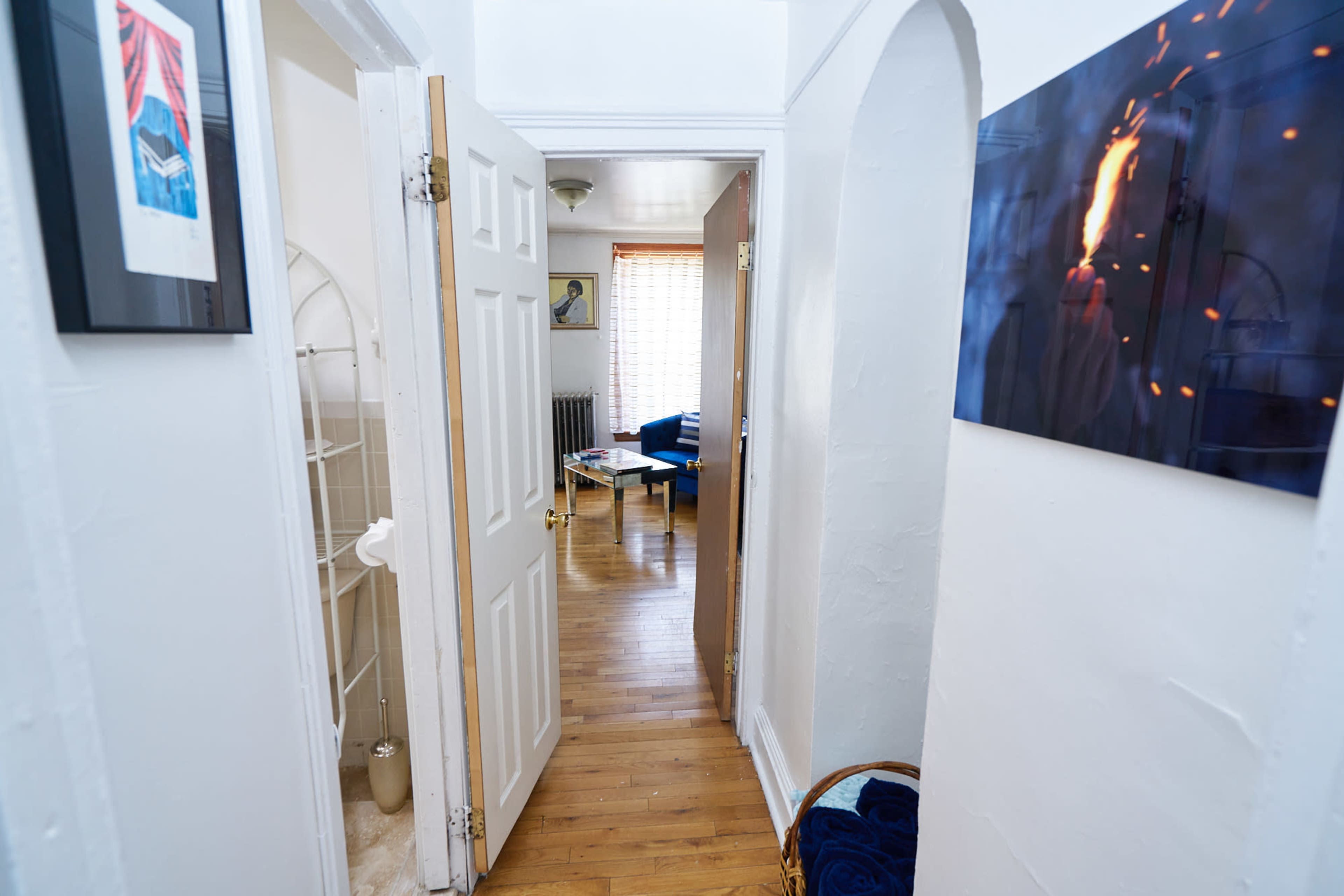 A hallway with white walls and wooden floors leads to a living area with a blue couch and a table.