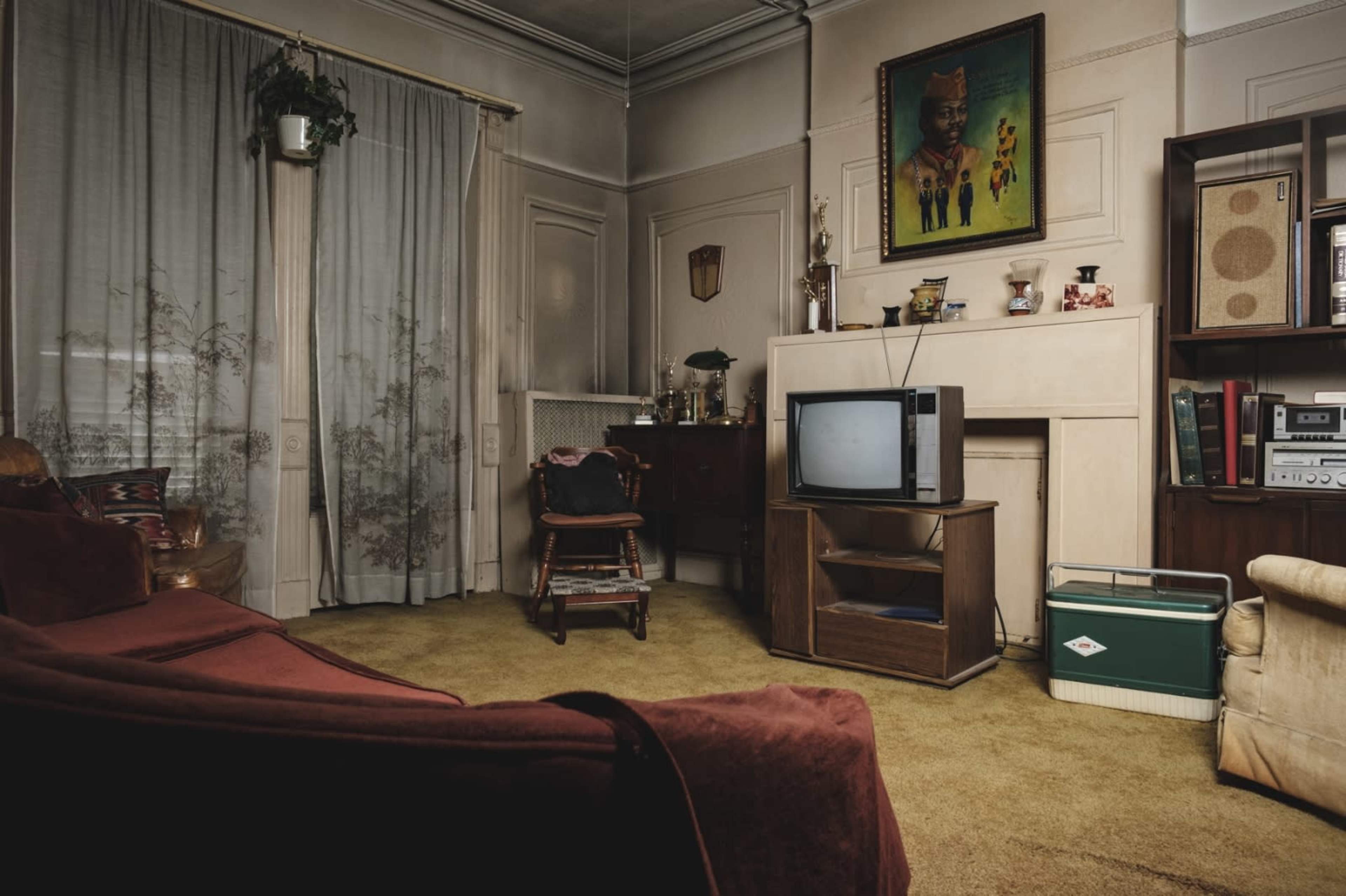 A vintage living room featuring a television on a wooden stand, a large painting on the wall, and a green cooler on the floor.