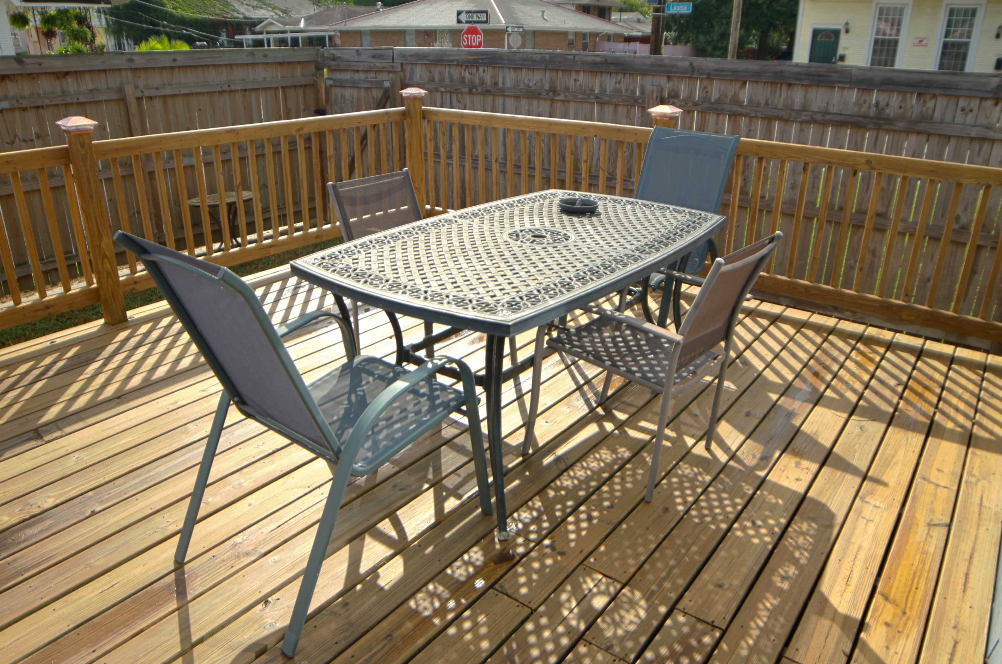 A metal table with four chairs is set on a wooden deck surrounded by a wooden fence.