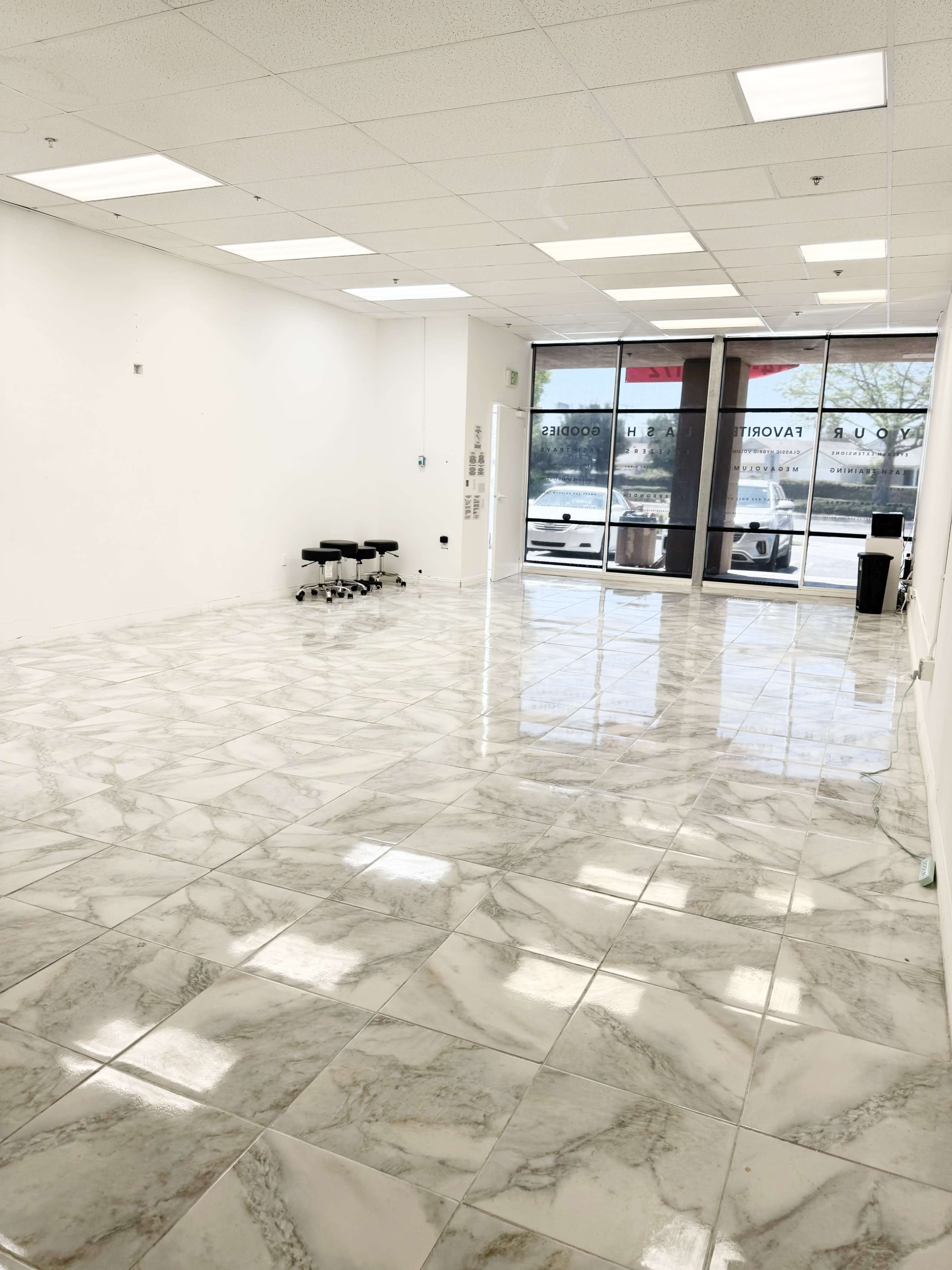 The image shows a spacious, empty room with marble-patterned tile flooring and large windows that let in natural light.