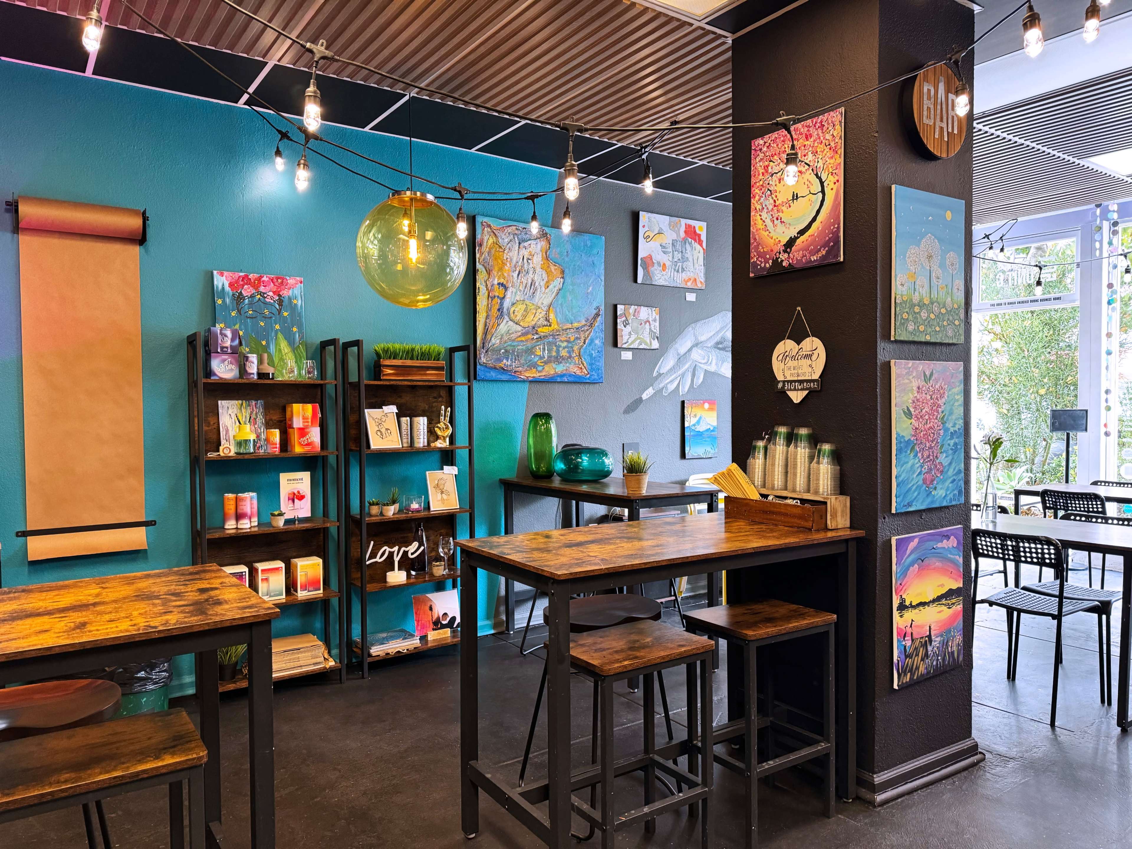 A vibrant café interior featuring colorful artwork on the walls, wooden tables and stools, and decorative lighting.