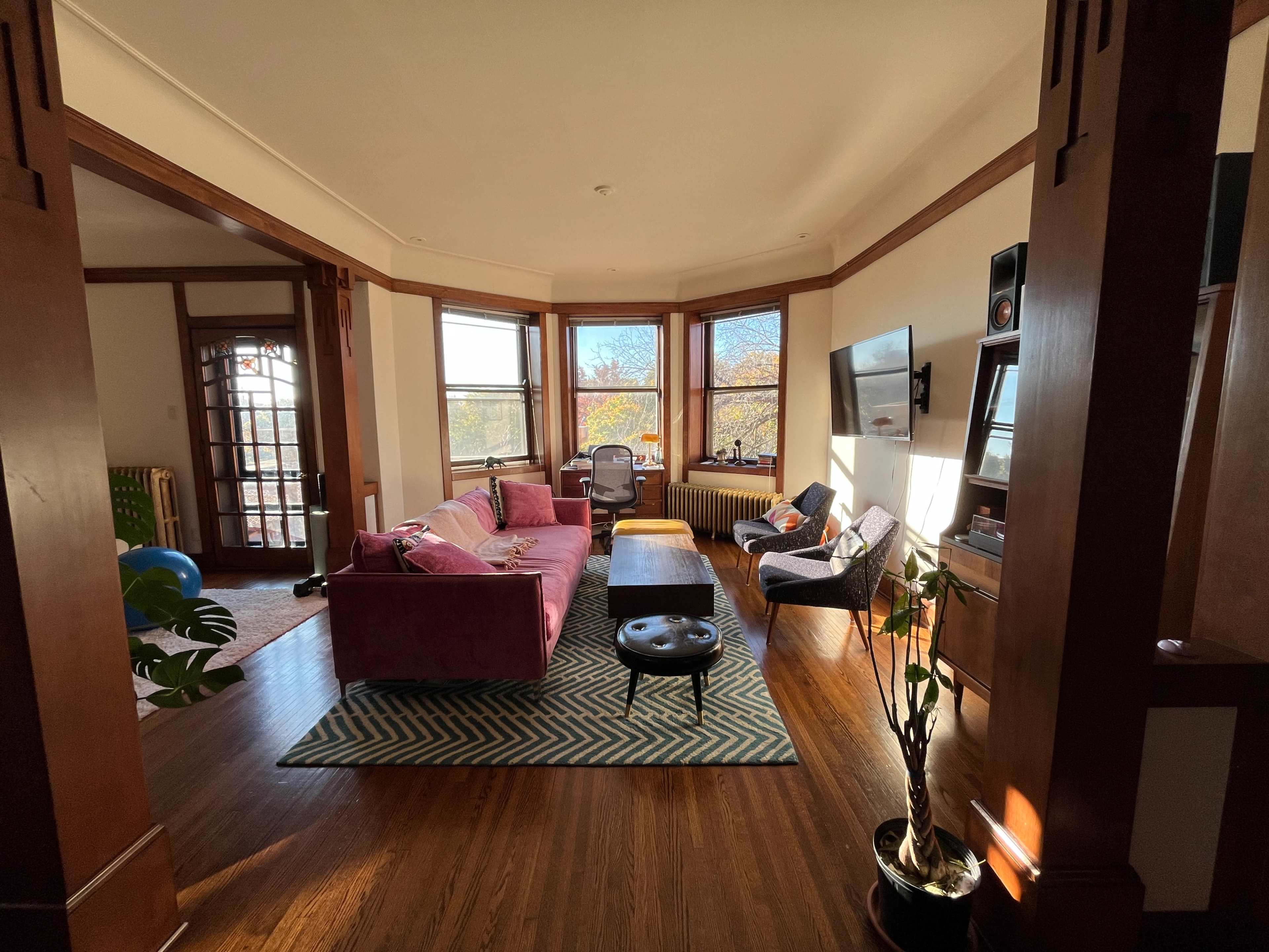 The image shows a spacious living room with a purple sofa, a coffee table, and large windows allowing natural light to fill the space.