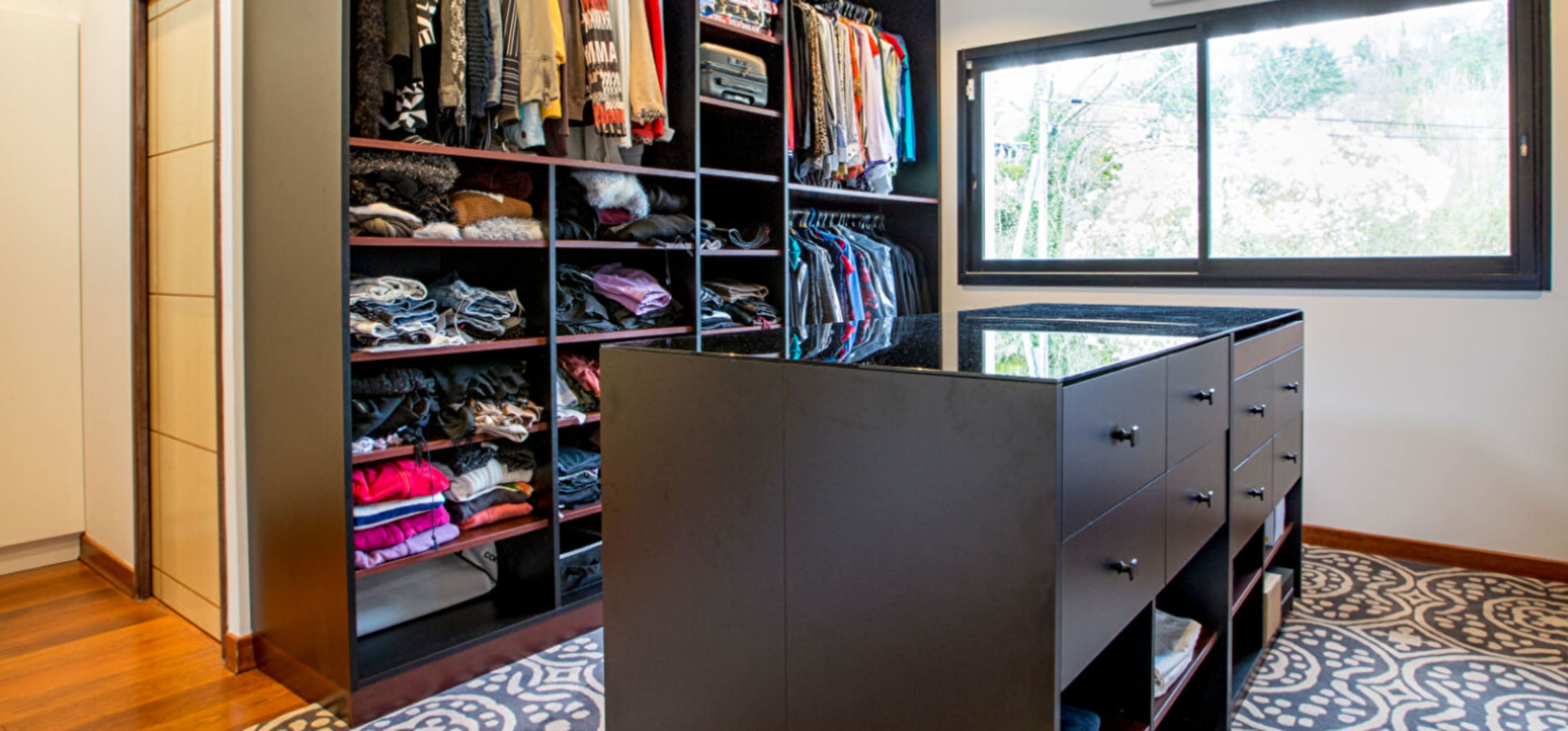 The image shows a well-organized walk-in closet featuring shelves of folded clothing and a central island with drawers.