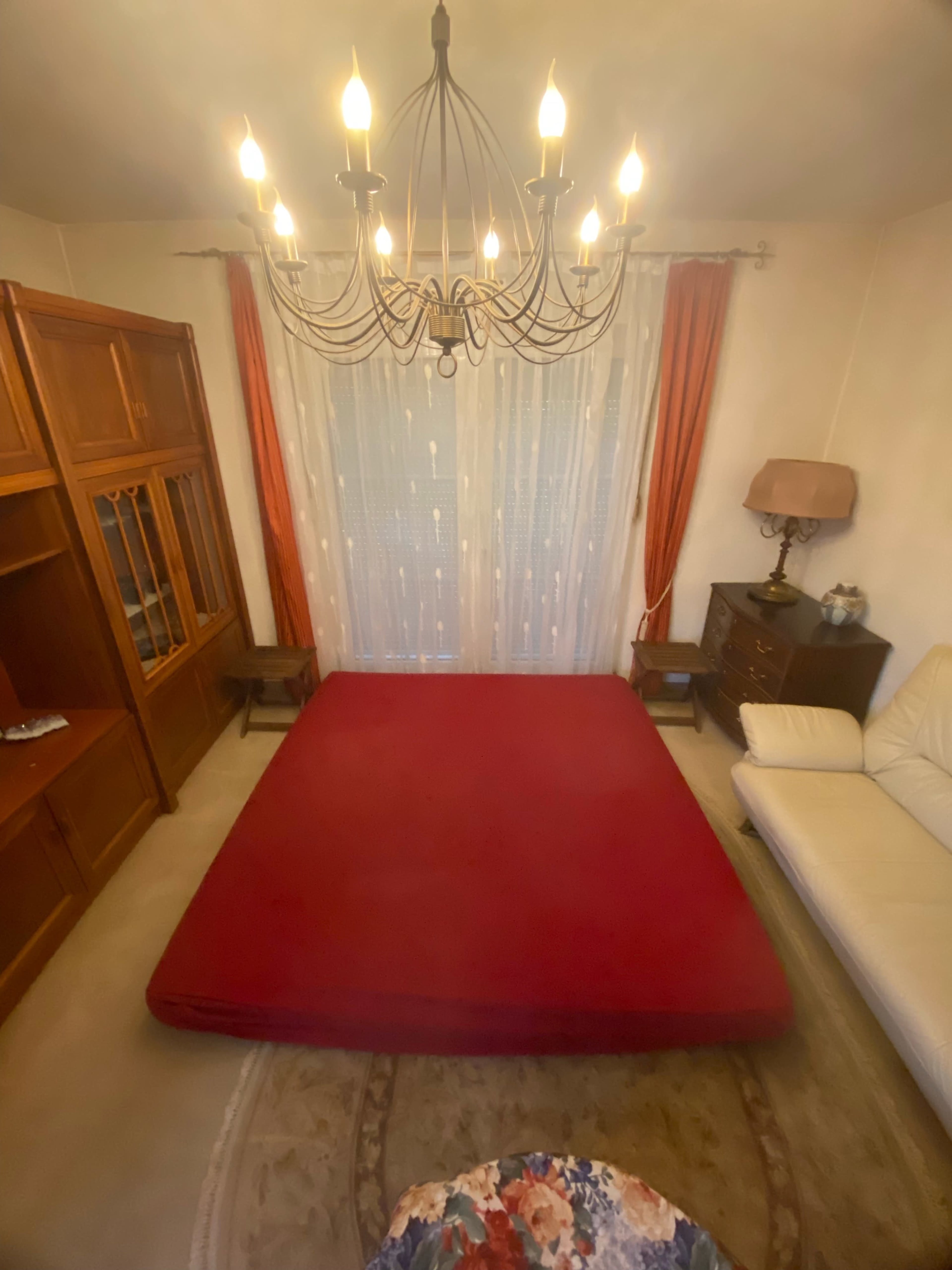 The image shows a room with a red mat on the floor, a chandelier overhead, and wooden furniture against the walls.