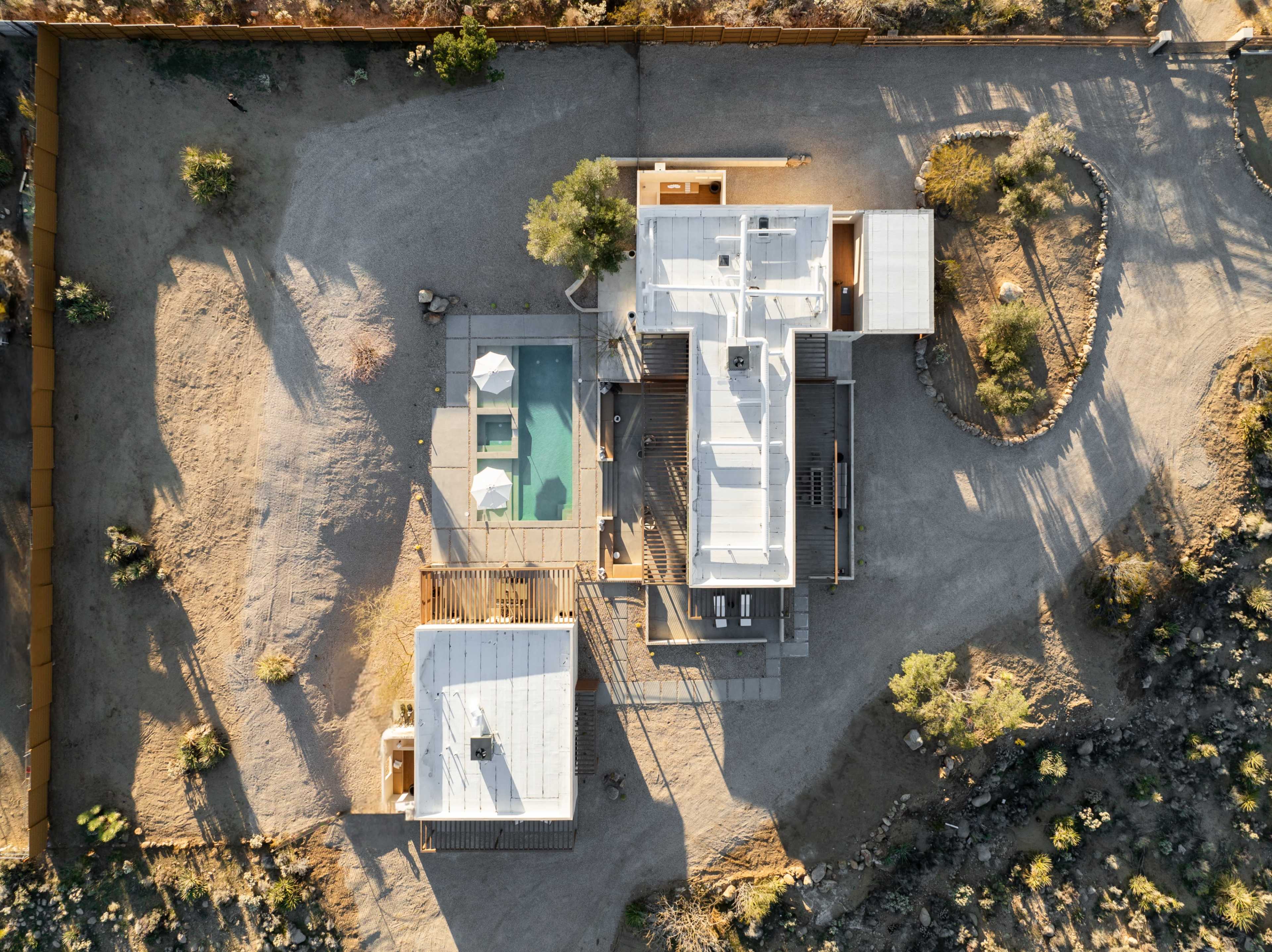 The image shows an aerial view of a modern residential complex with multiple structures, a swimming pool, and surrounding desert landscape.