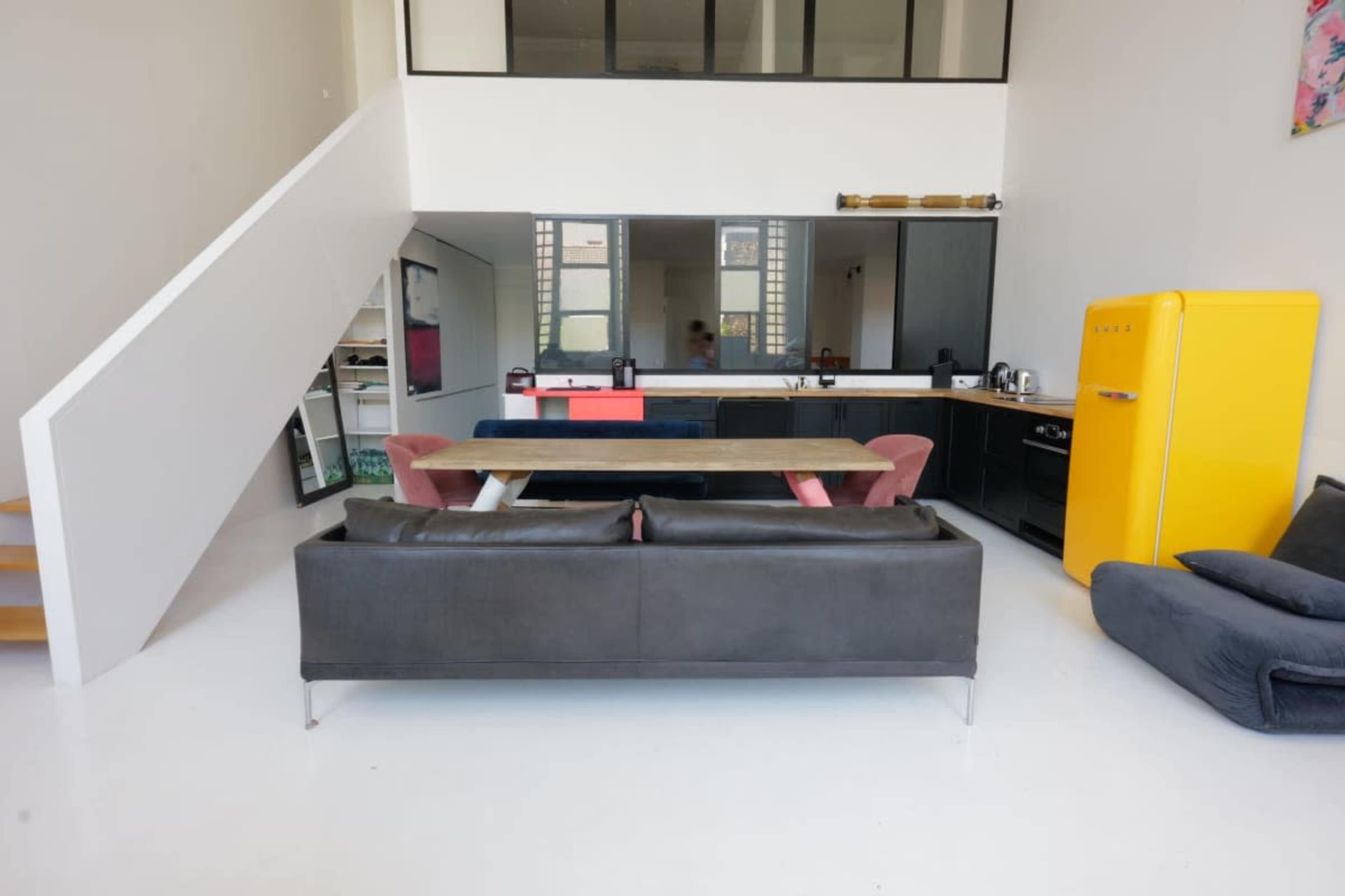 The image shows a modern, open-concept living space with a kitchen, dining area, and seating, featuring a black sofa and a yellow refrigerator.