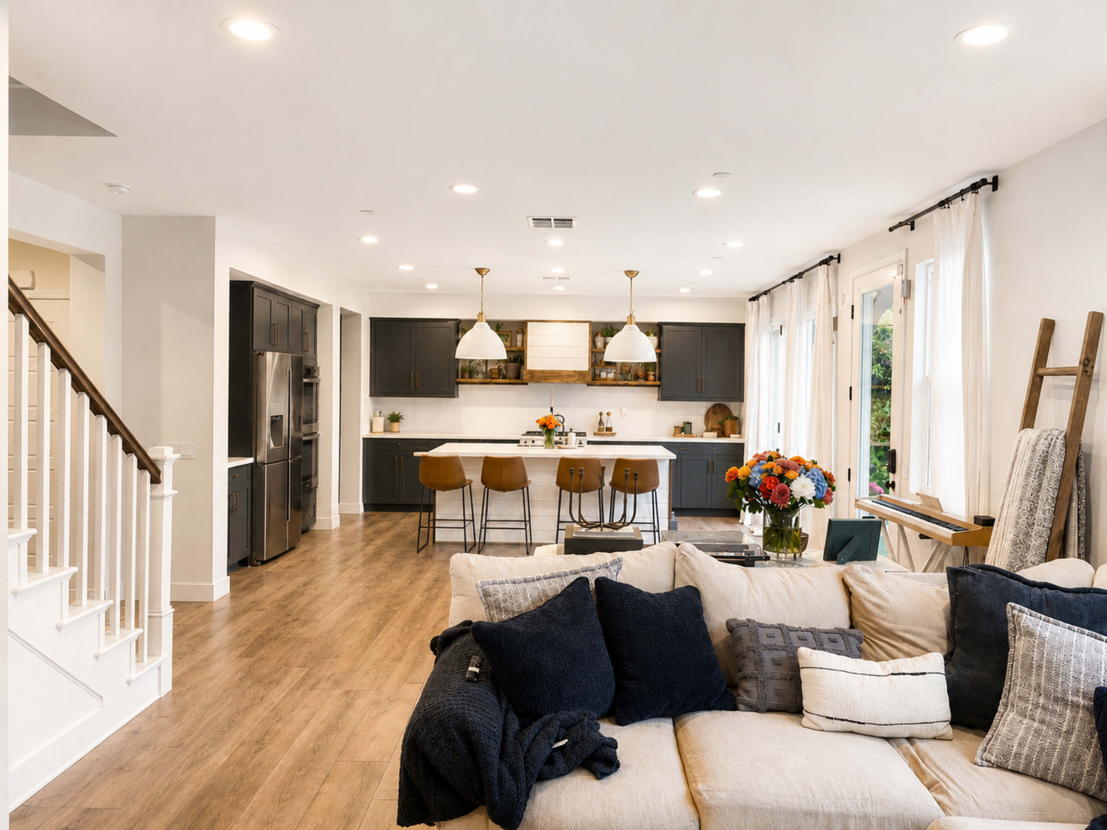 A modern kitchen and living area features a spacious open layout with dark cabinetry, a large island with bar stools, and a cozy sofa with decorative cushions.