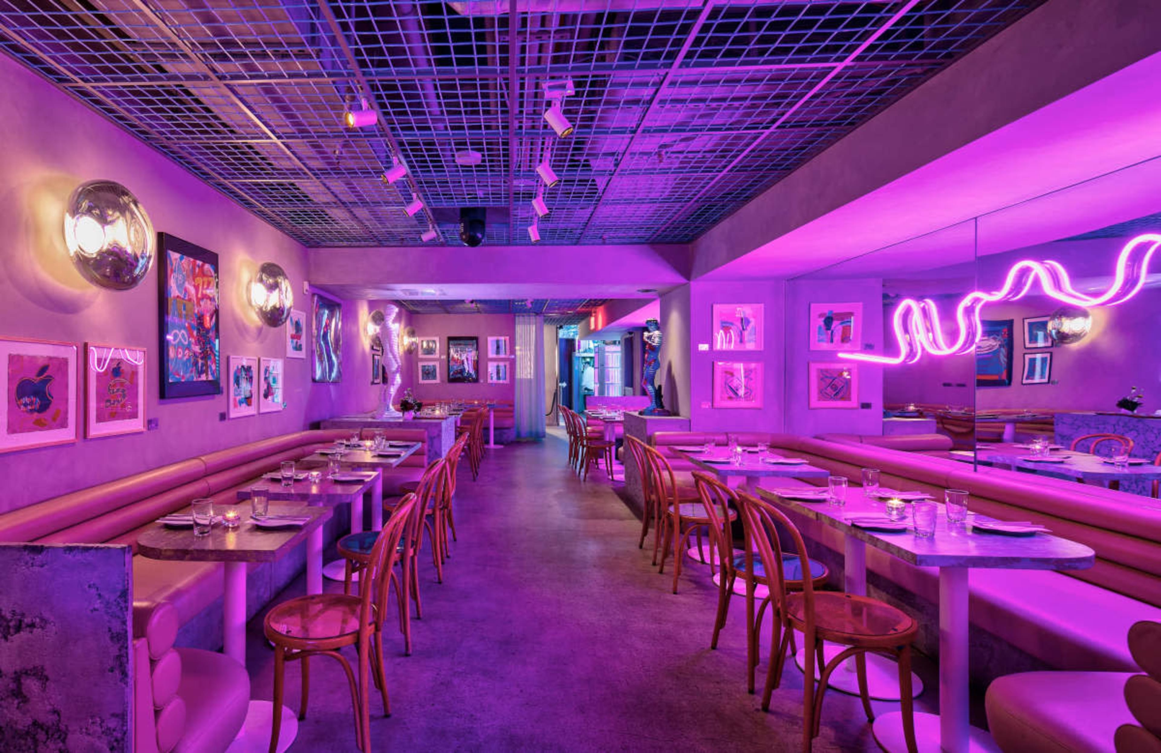 The image shows a modern restaurant interior with pink lighting, featuring wooden chairs, circular tables, and artwork displayed on the walls.