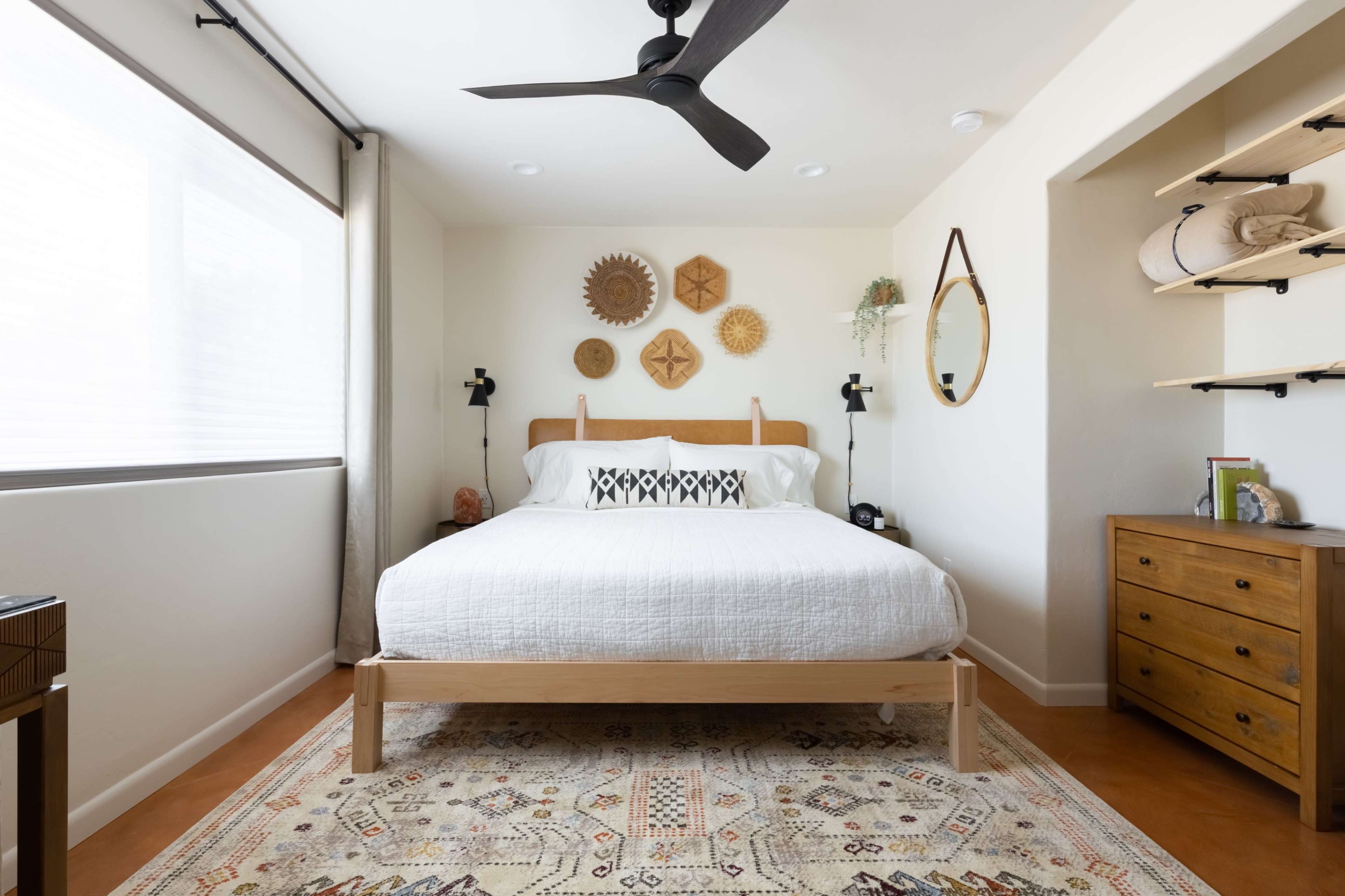 A well-organized bedroom featuring a wooden bed, decorative wall hangings, and a nightstand beside a large window.