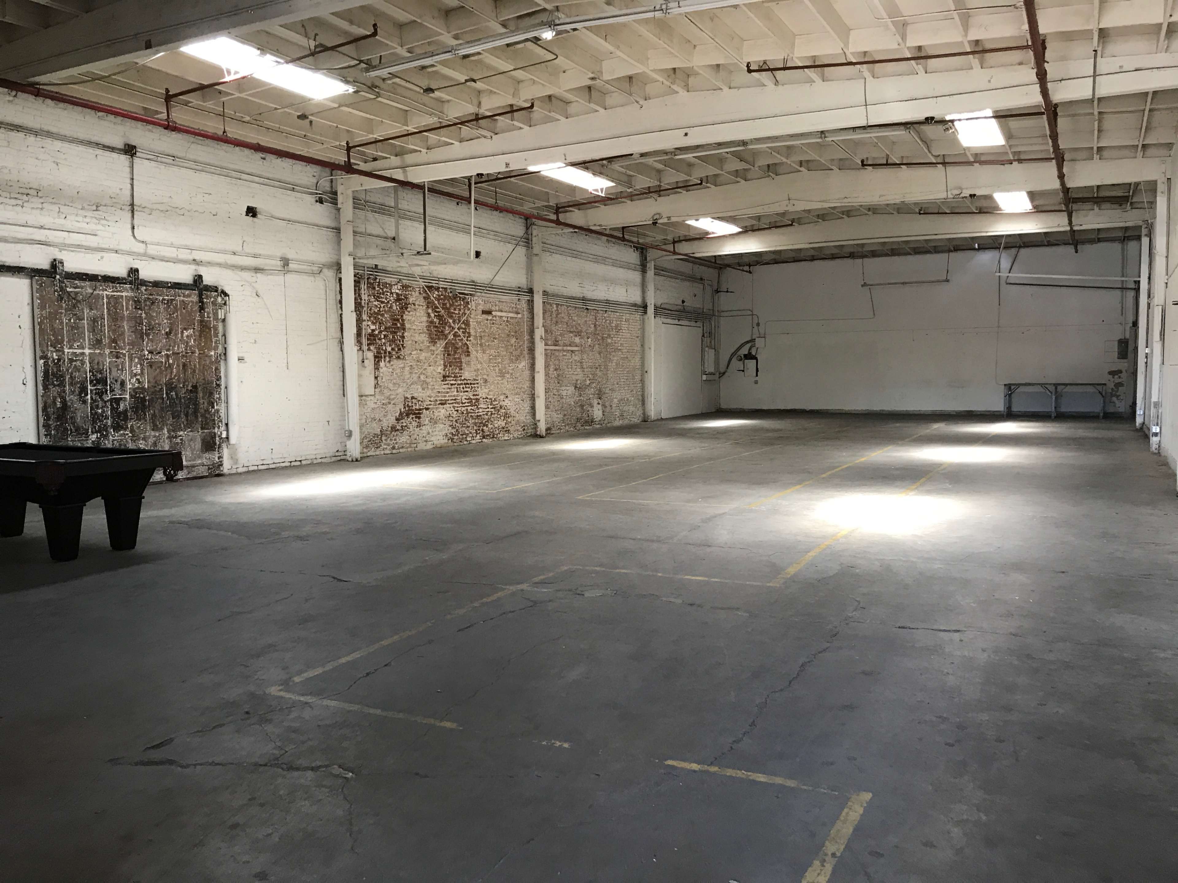 A spacious, empty warehouse with concrete flooring and exposed brick walls.
