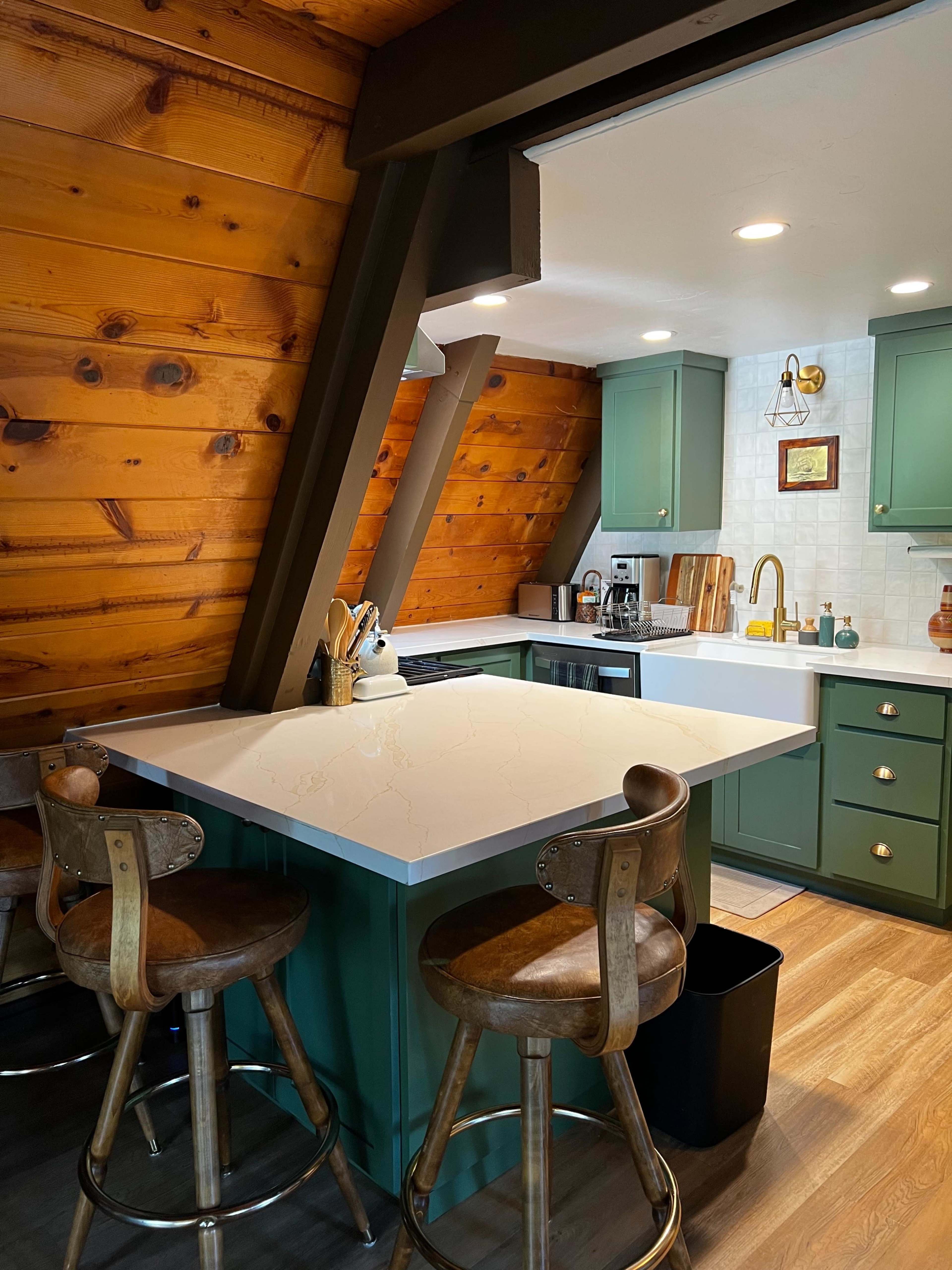 A kitchen with an A-frame ceiling, featuring green cabinets, a white countertop, and wooden walls.