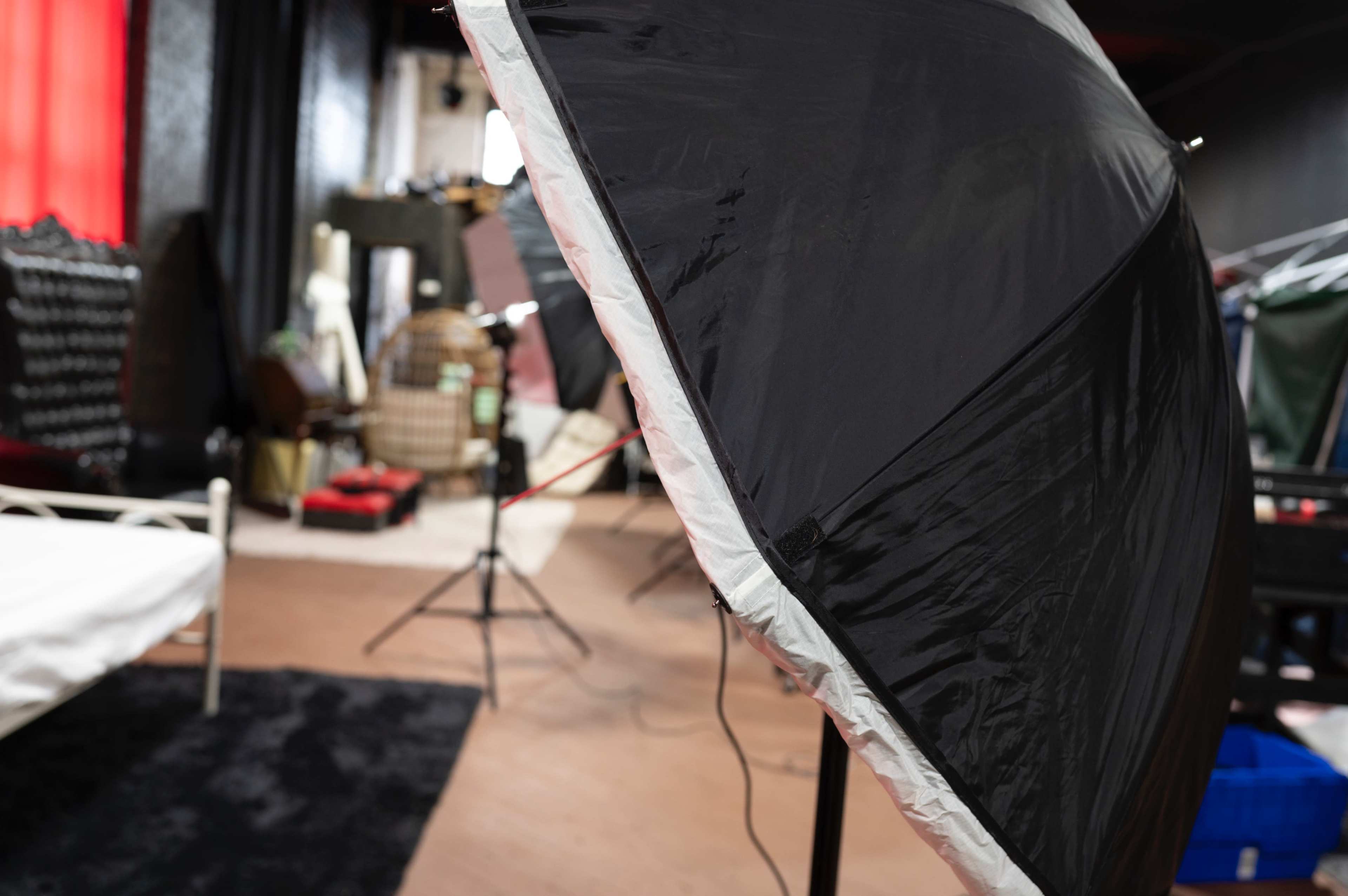 A black umbrella softbox is positioned in a dimly lit studio with various equipment and props in the background.