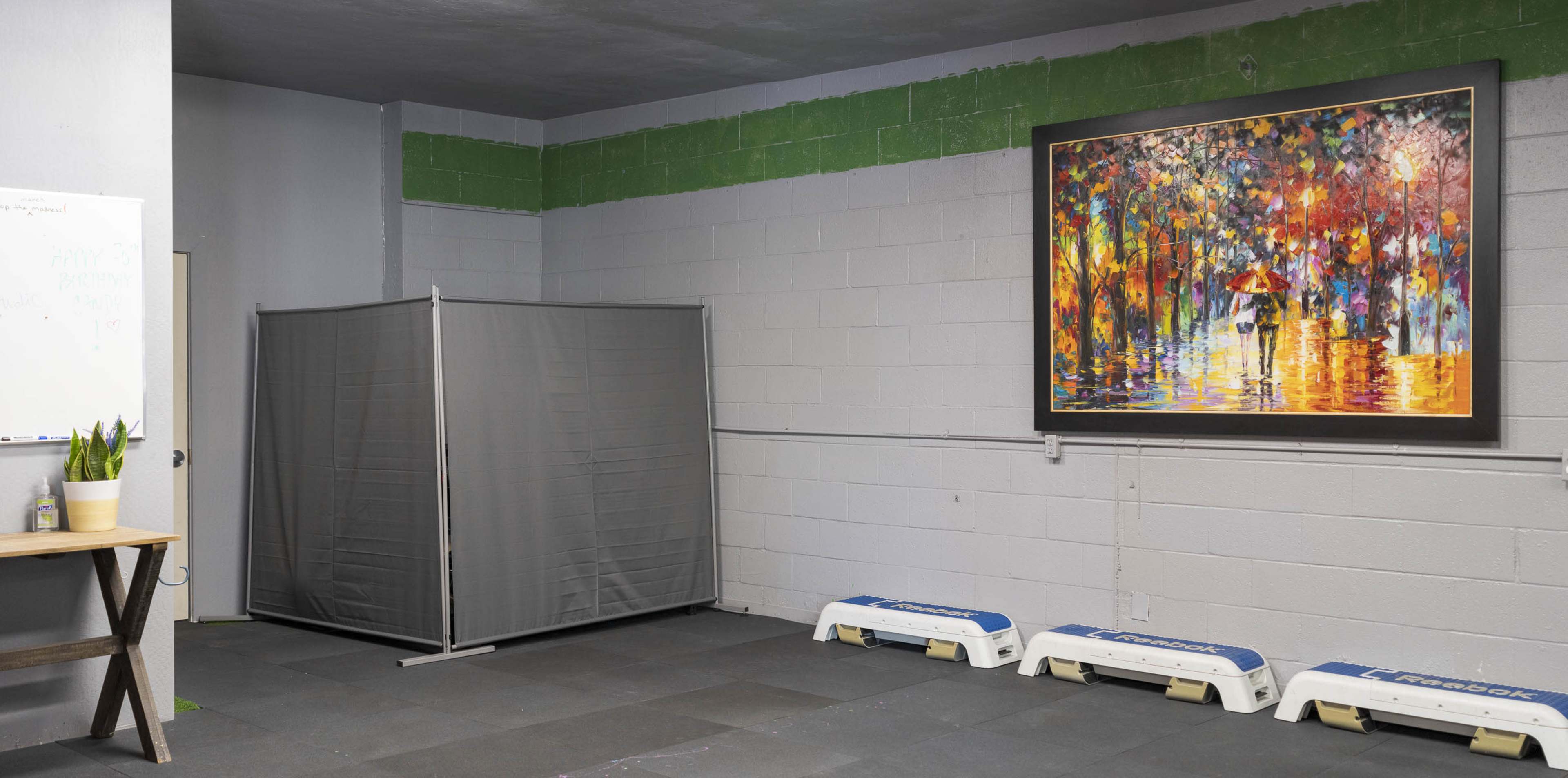 A minimalist room with gray walls, a large colorful painting on the wall, a gray partition, and a few white exercise platforms on the floor.