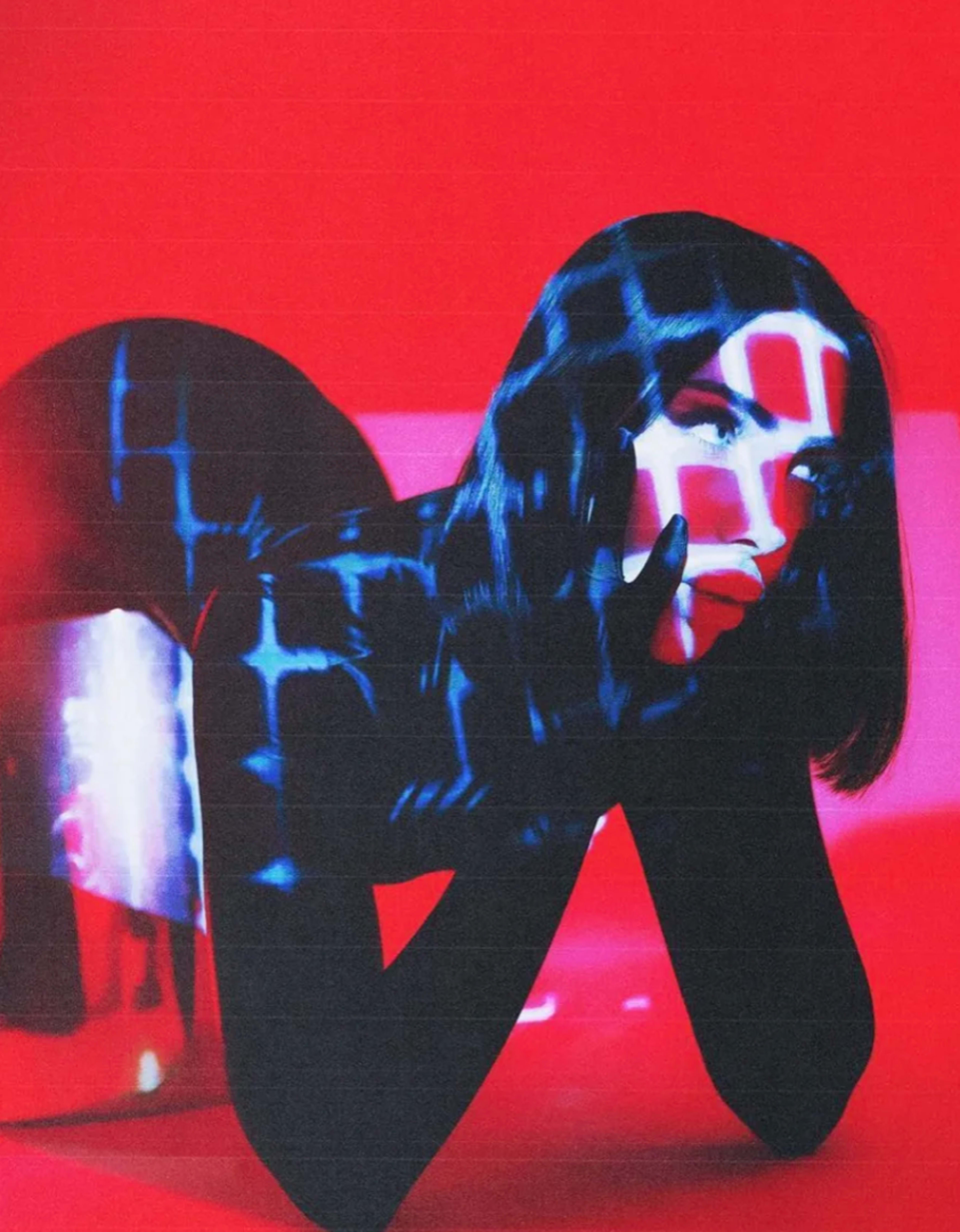 A figure in black clothing poses with a hand on their face while colored light patterns project onto their body against a red background.