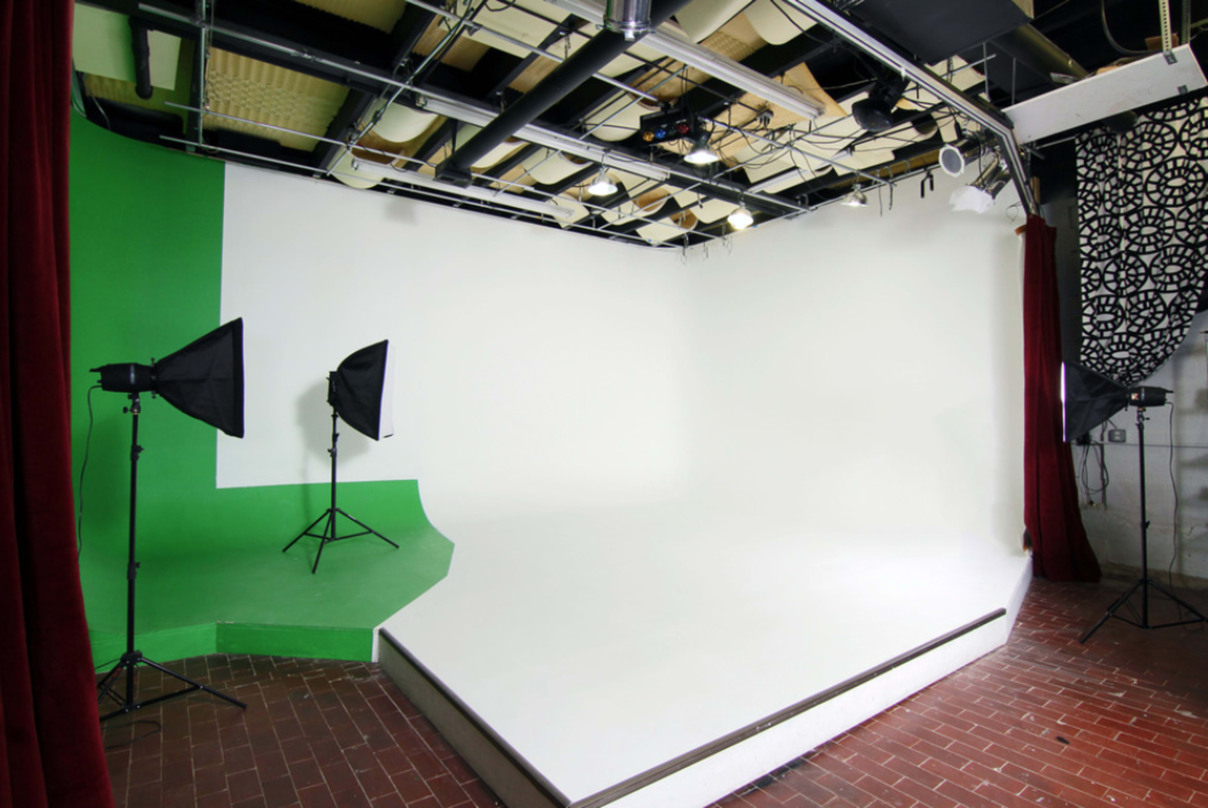 The image shows a photography studio with a green corner, white backdrop, and two softbox lights on stands.