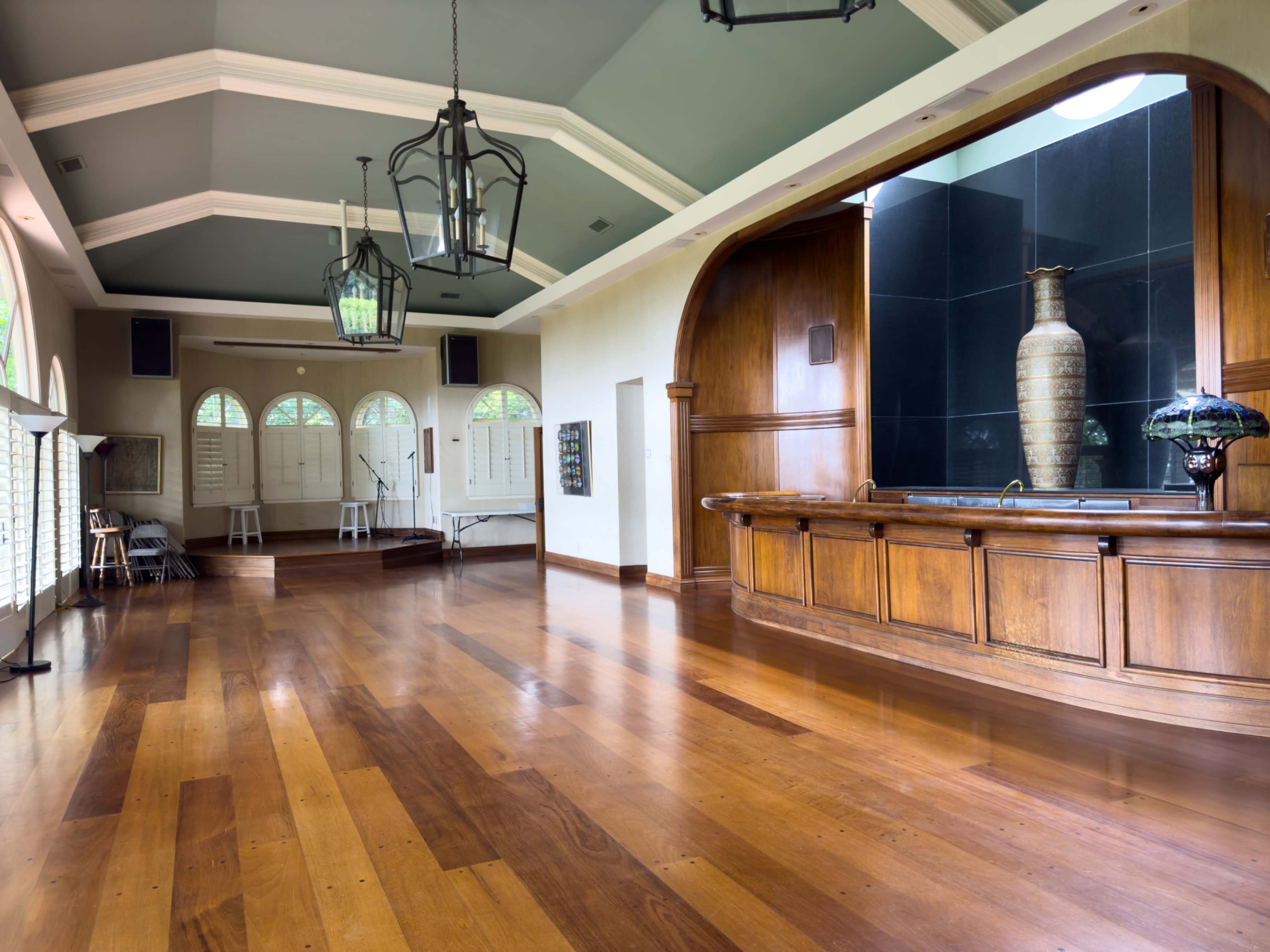 The image shows a spacious interior with hardwood floors, large windows, and a wooden bar area featuring a decorative vase and wall paneling.