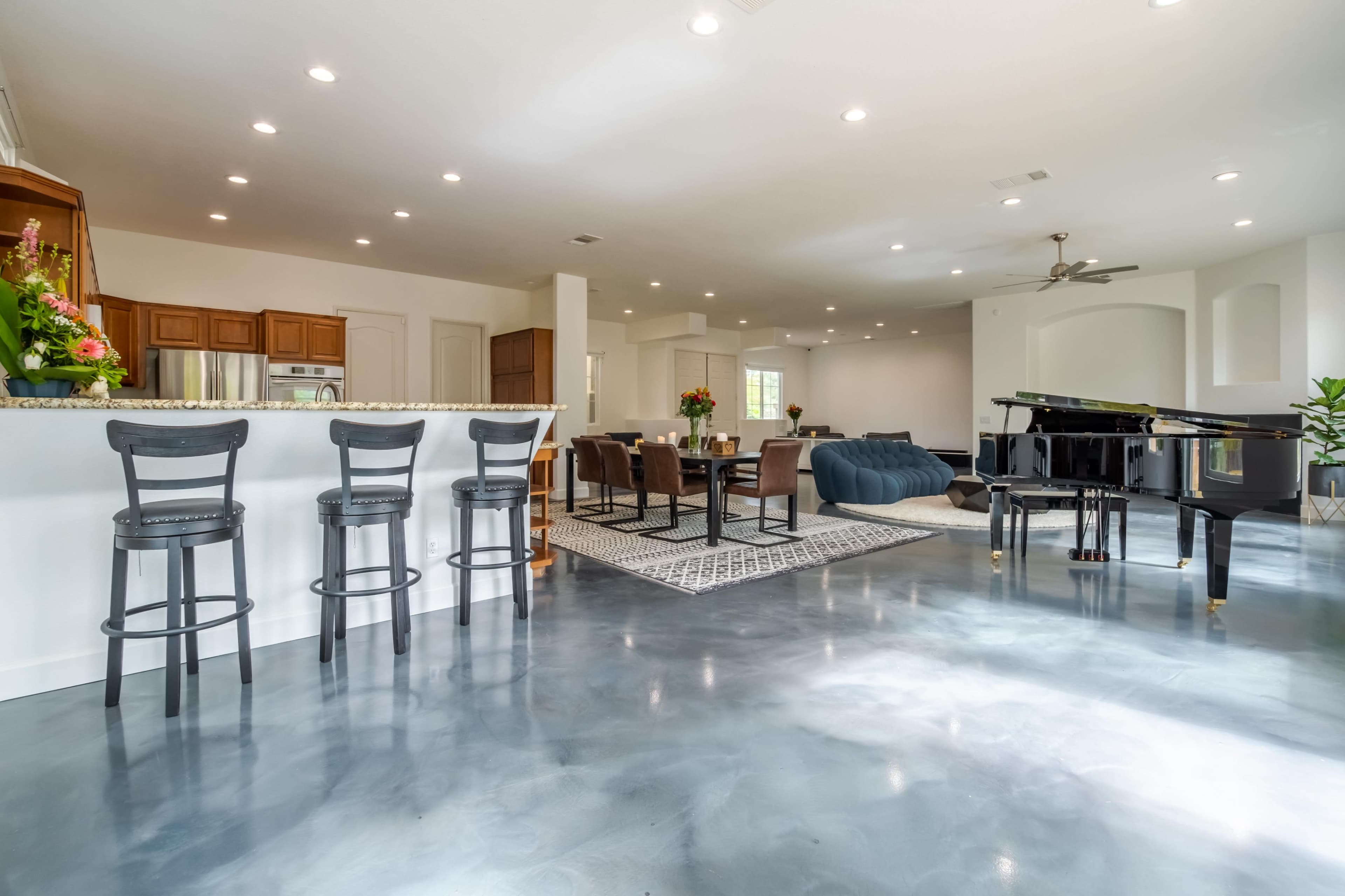A spacious open-concept living area features a kitchen bar with four chairs, a grand piano, and a dining area adjacent to a cozy seating space.