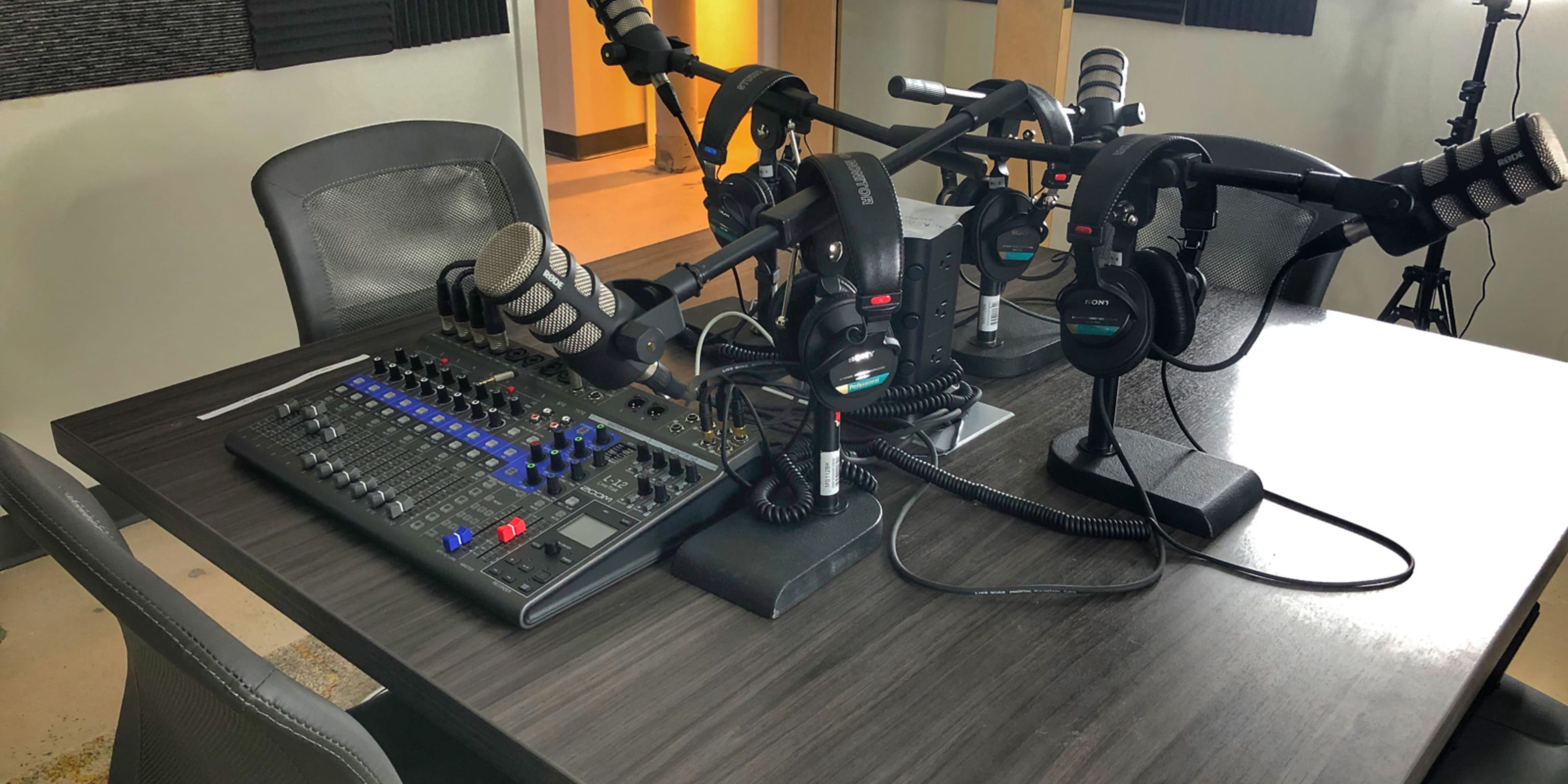 A radio studio setup featuring a mixing console and several headsets on a table with microphone stands.