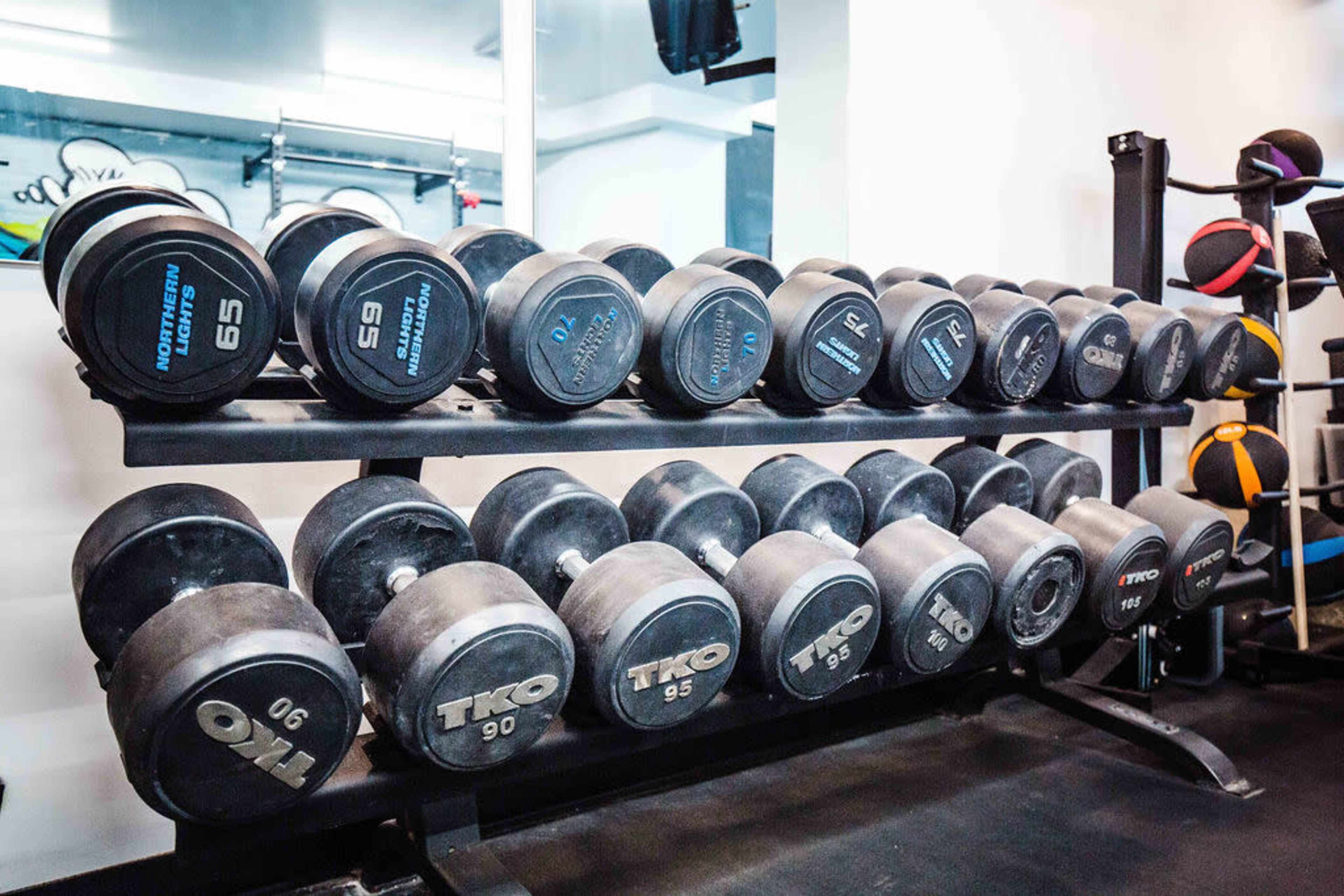 A rack displays various sizes of dumbbells in a gym setting.