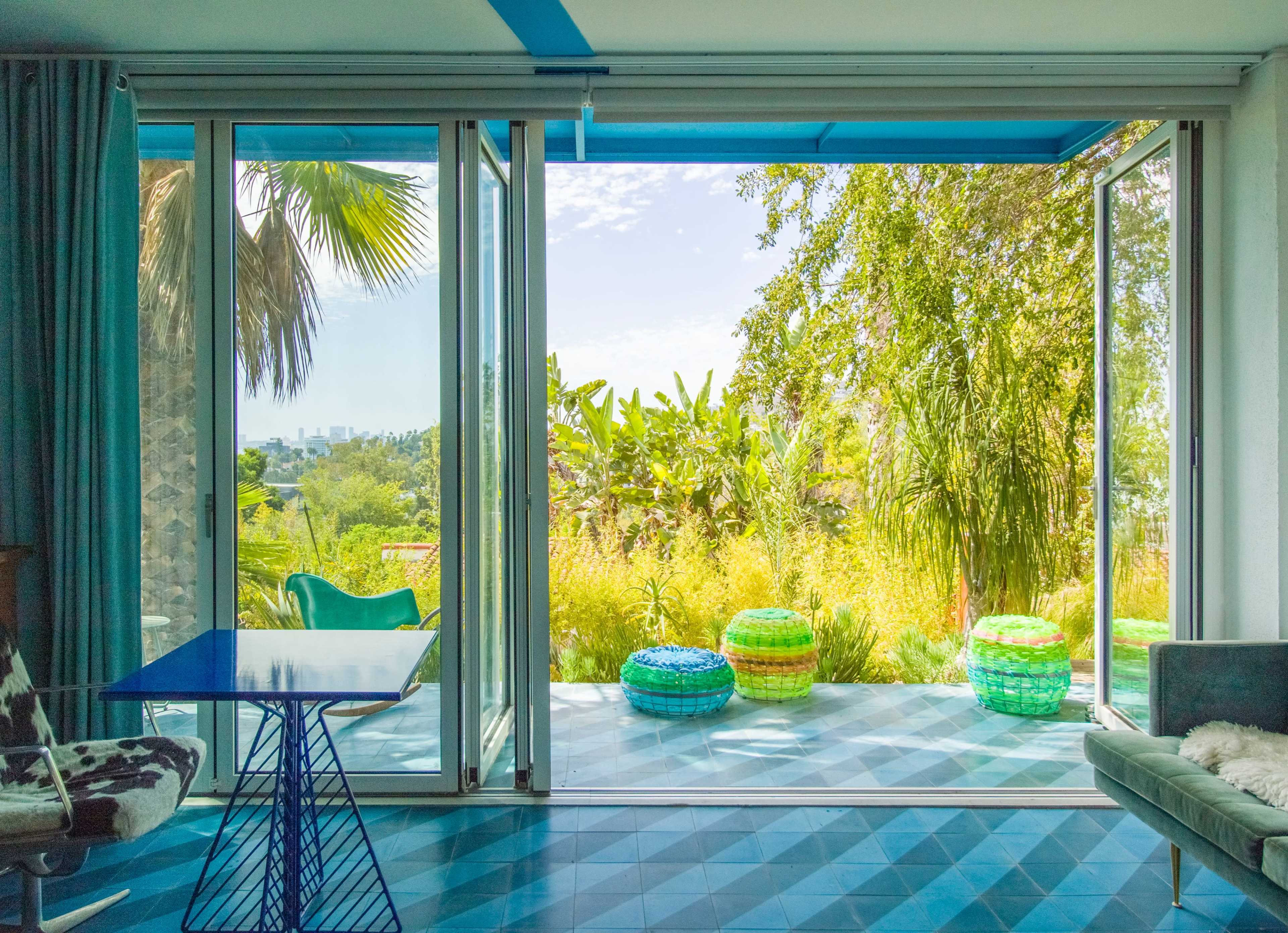 A modern room features large glass doors opening to a lush garden with colorful circular seating and vibrant greenery.