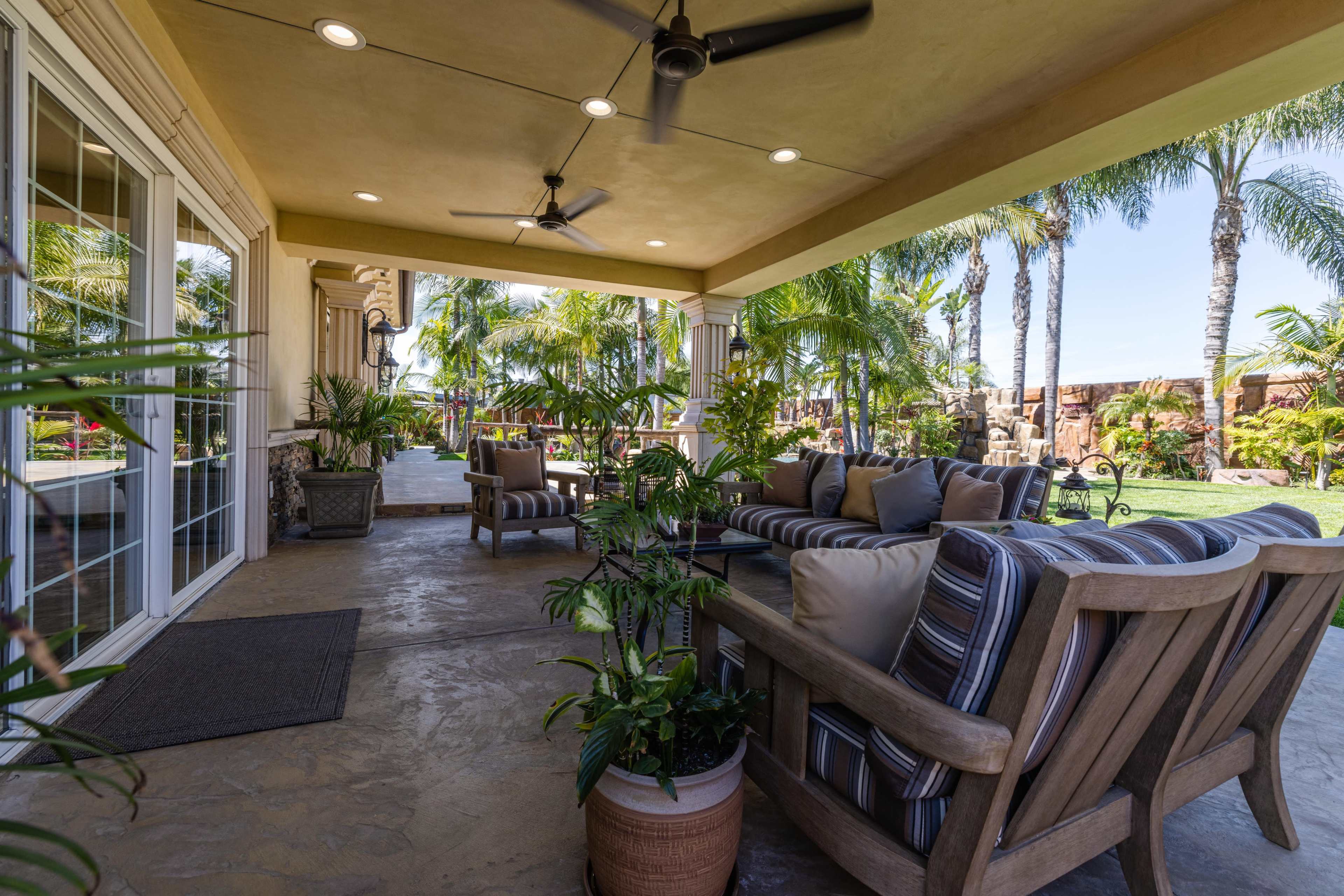 A covered patio area with comfortable seating, surrounding palm trees, and a well-maintained lawn.