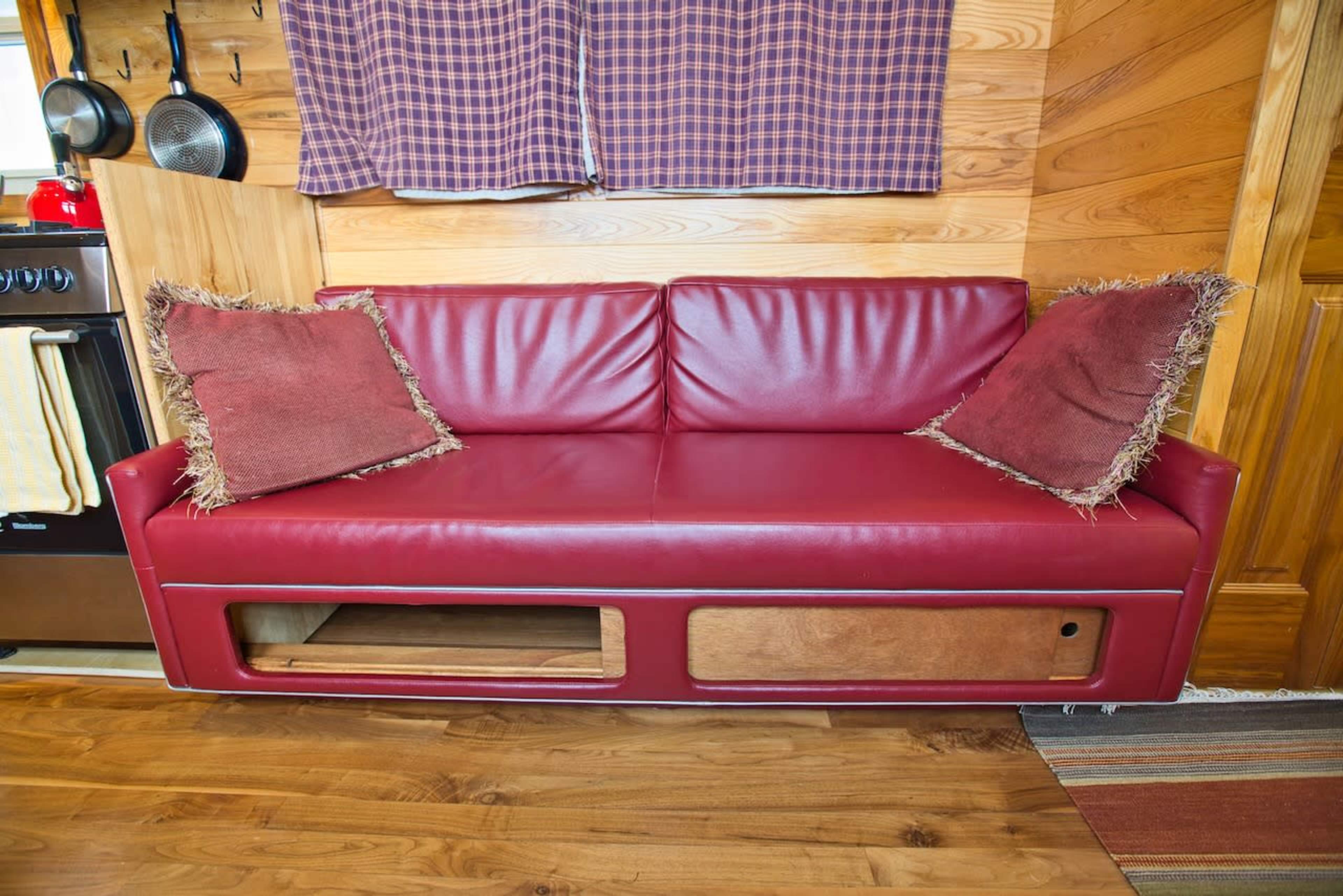 A red leather couch with two decorative pillows, positioned against a wooden wall in a kitchen area.