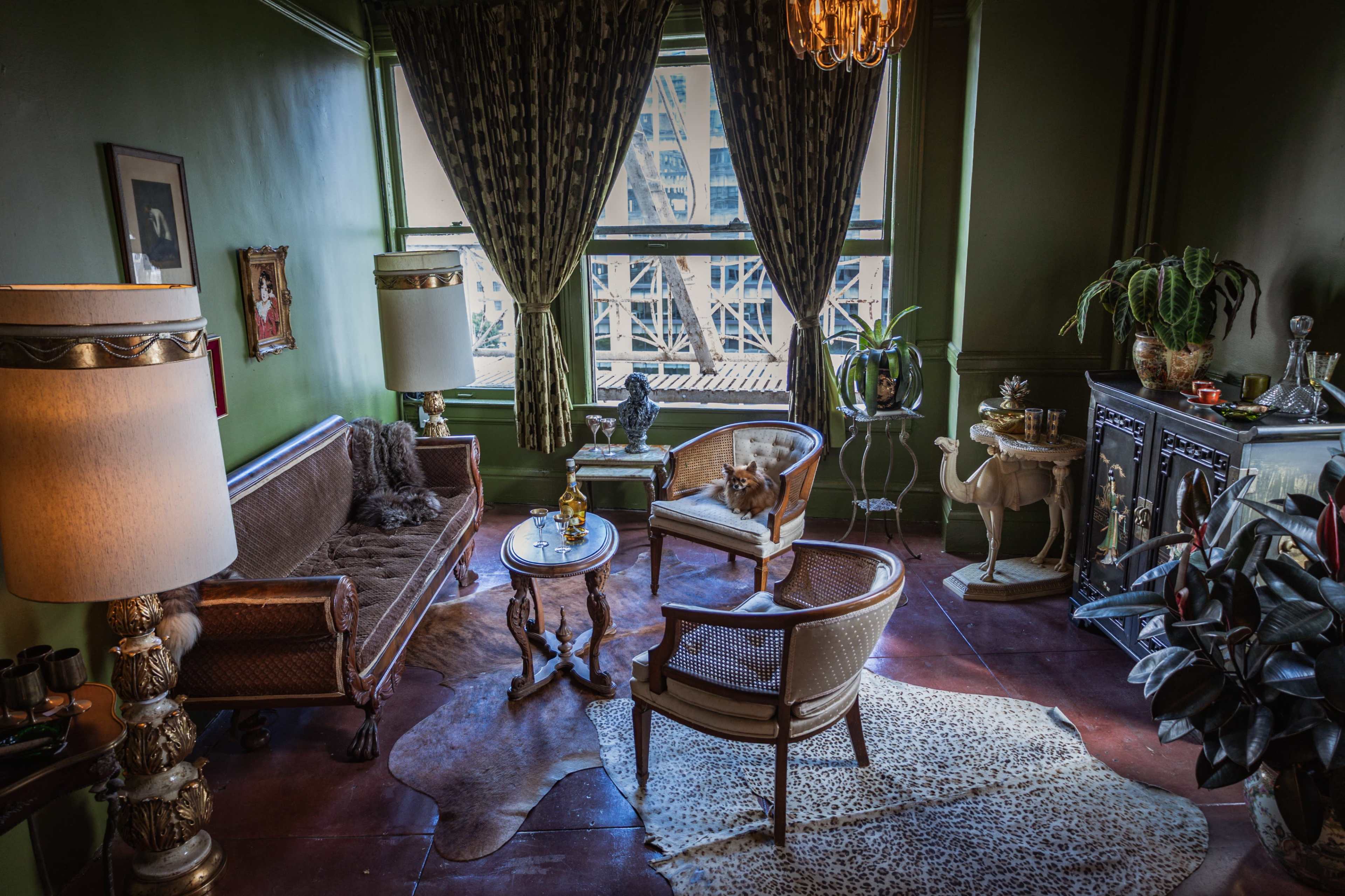 The room features vintage furniture, a large window with a view, and a mix of decorative items, creating a cozy yet elegant atmosphere.