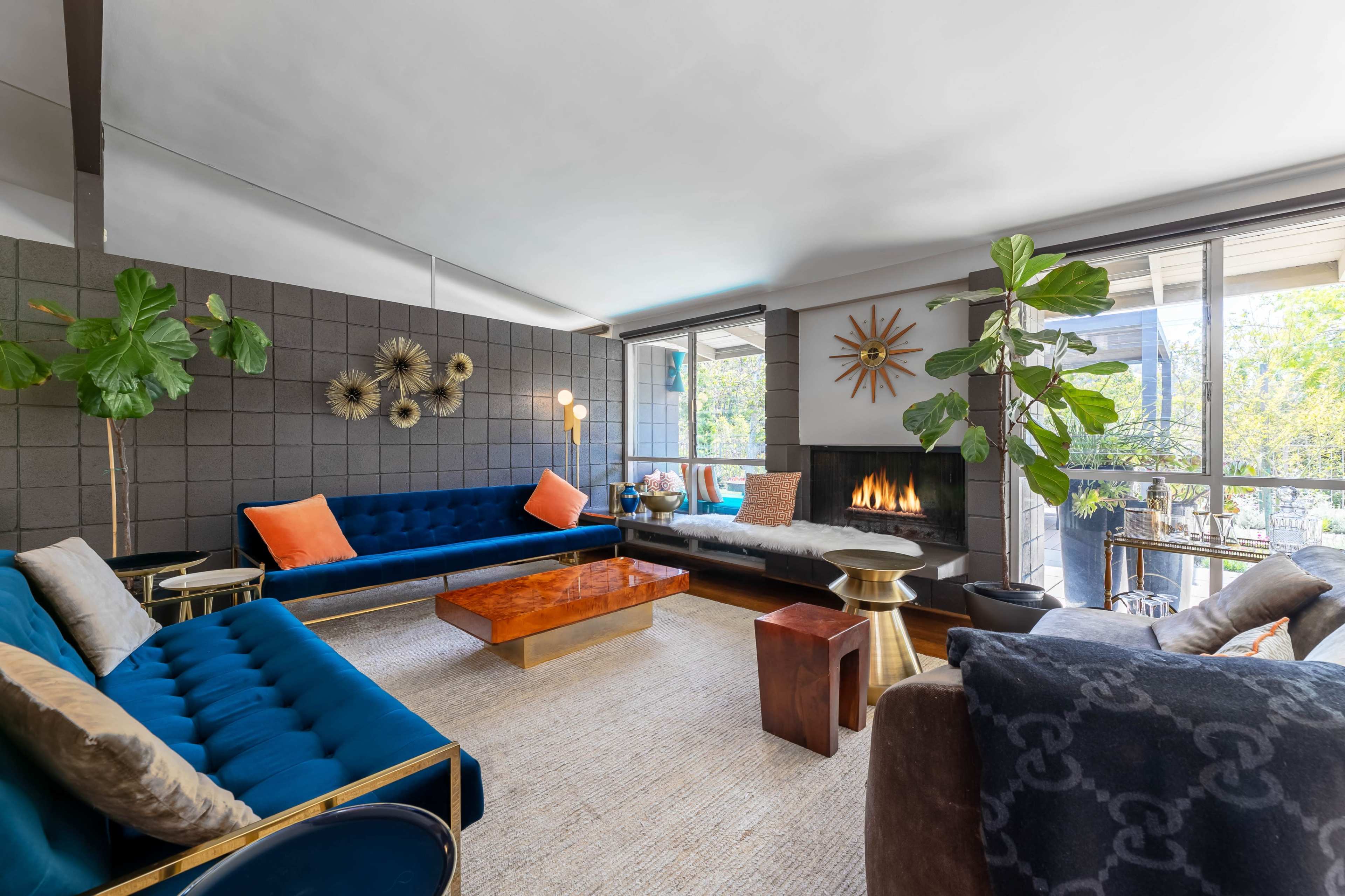 A modern living room features two blue sofas, a wooden coffee table, and large windows allowing natural light to fill the space.