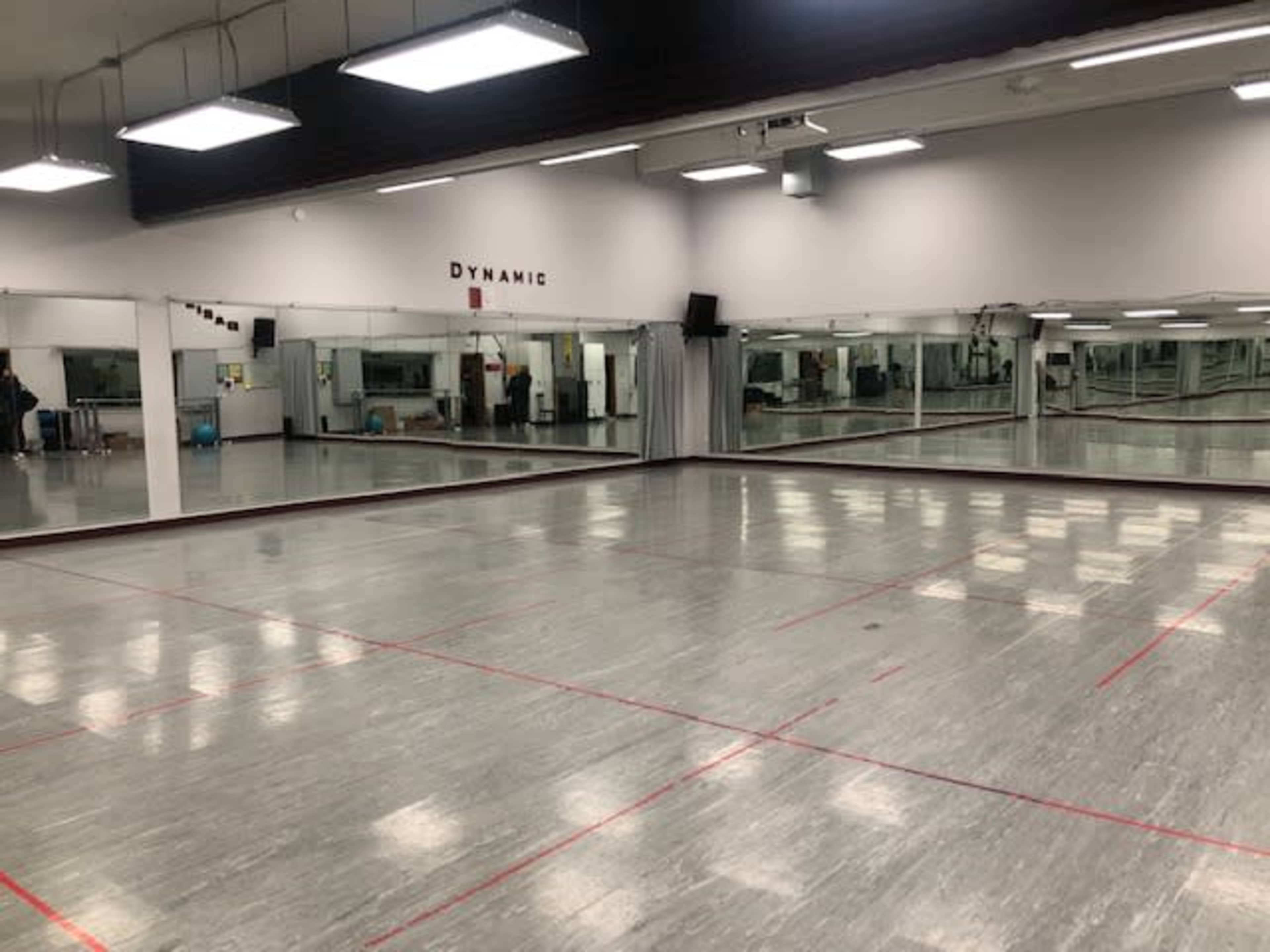 A spacious dance studio with mirrored walls, wooden flooring, and red tape markings on the ground.