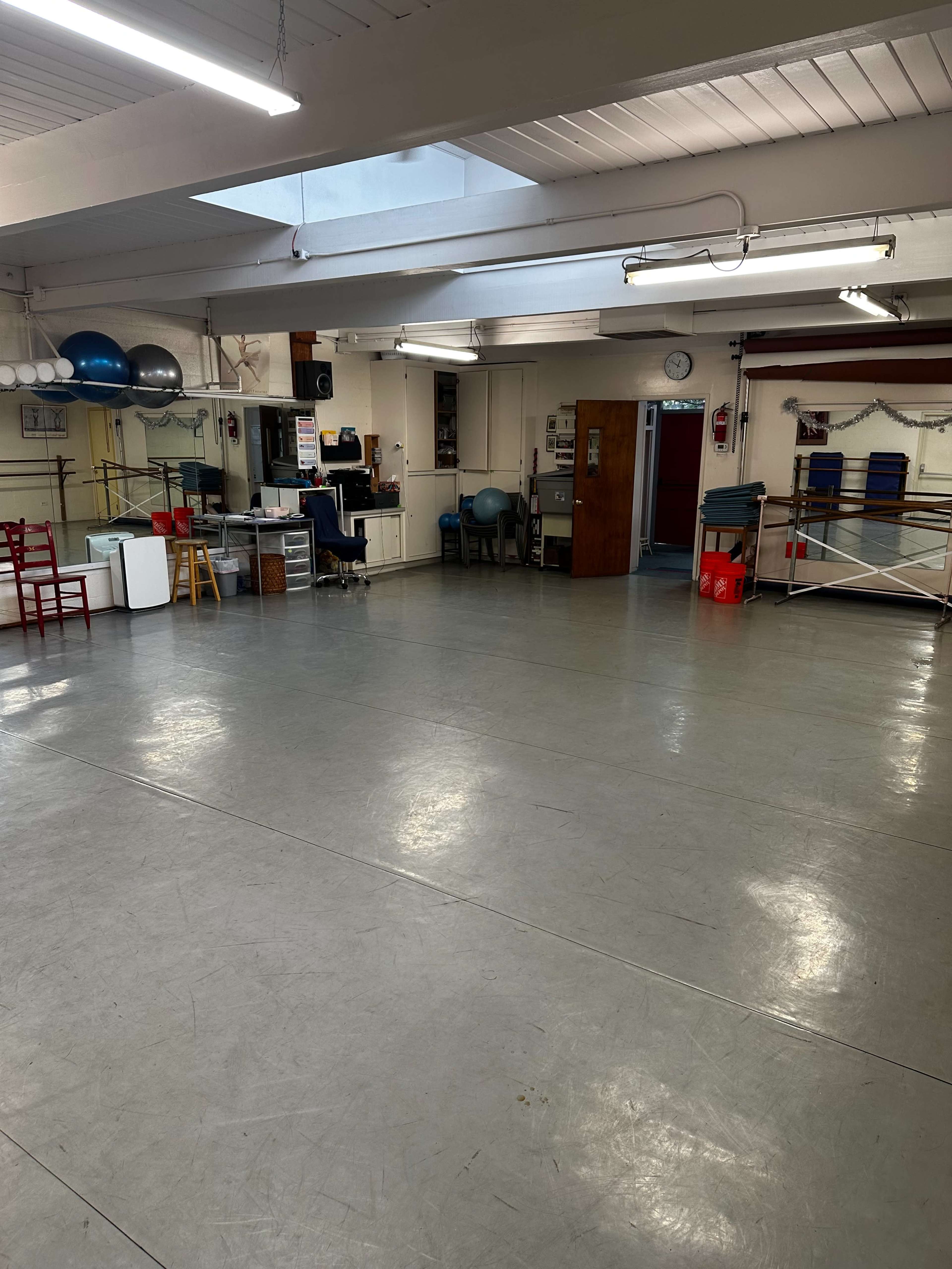 The image shows a spacious, well-lit interior of a studio or gym with various equipment, including exercise balls and chairs, arranged around the room.