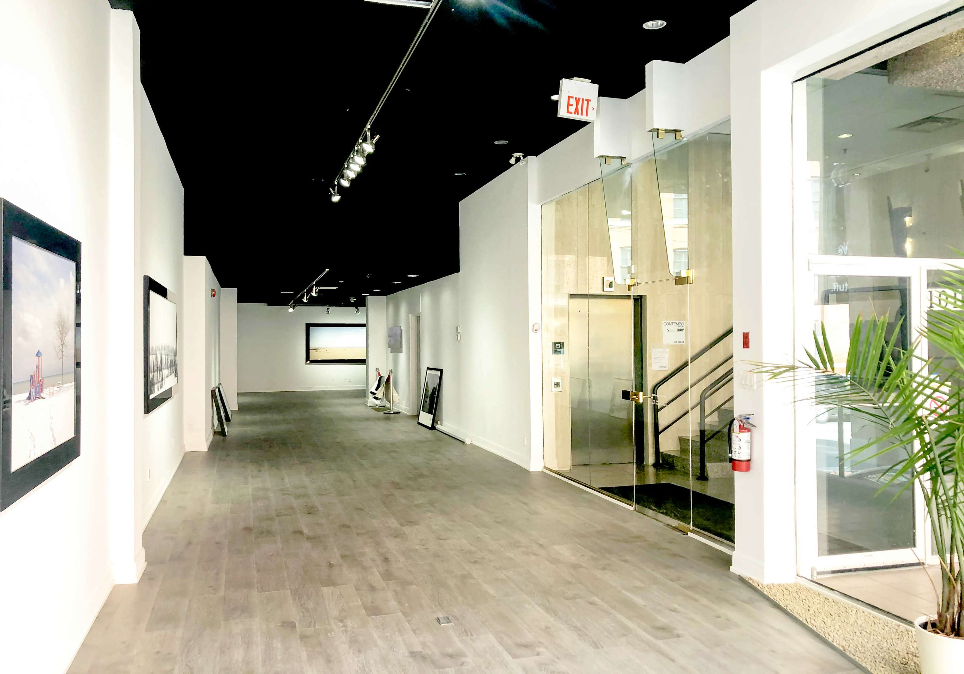 A well-lit hallway in an art gallery with large framed artworks on the walls and a glass entrance door at the end.