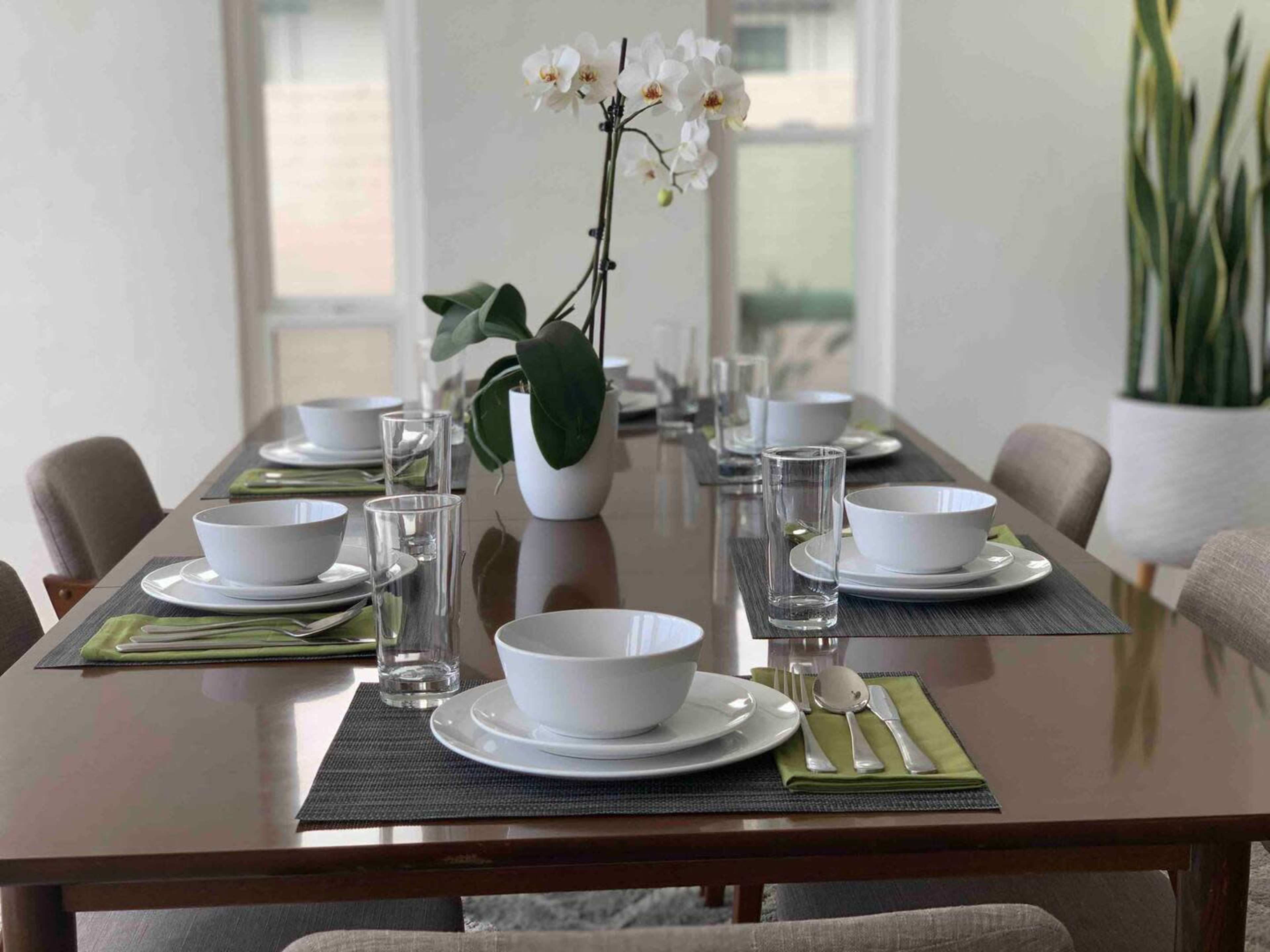 A dining table is set with white dishes, green napkins, glassware, and a decorative orchid centerpiece.